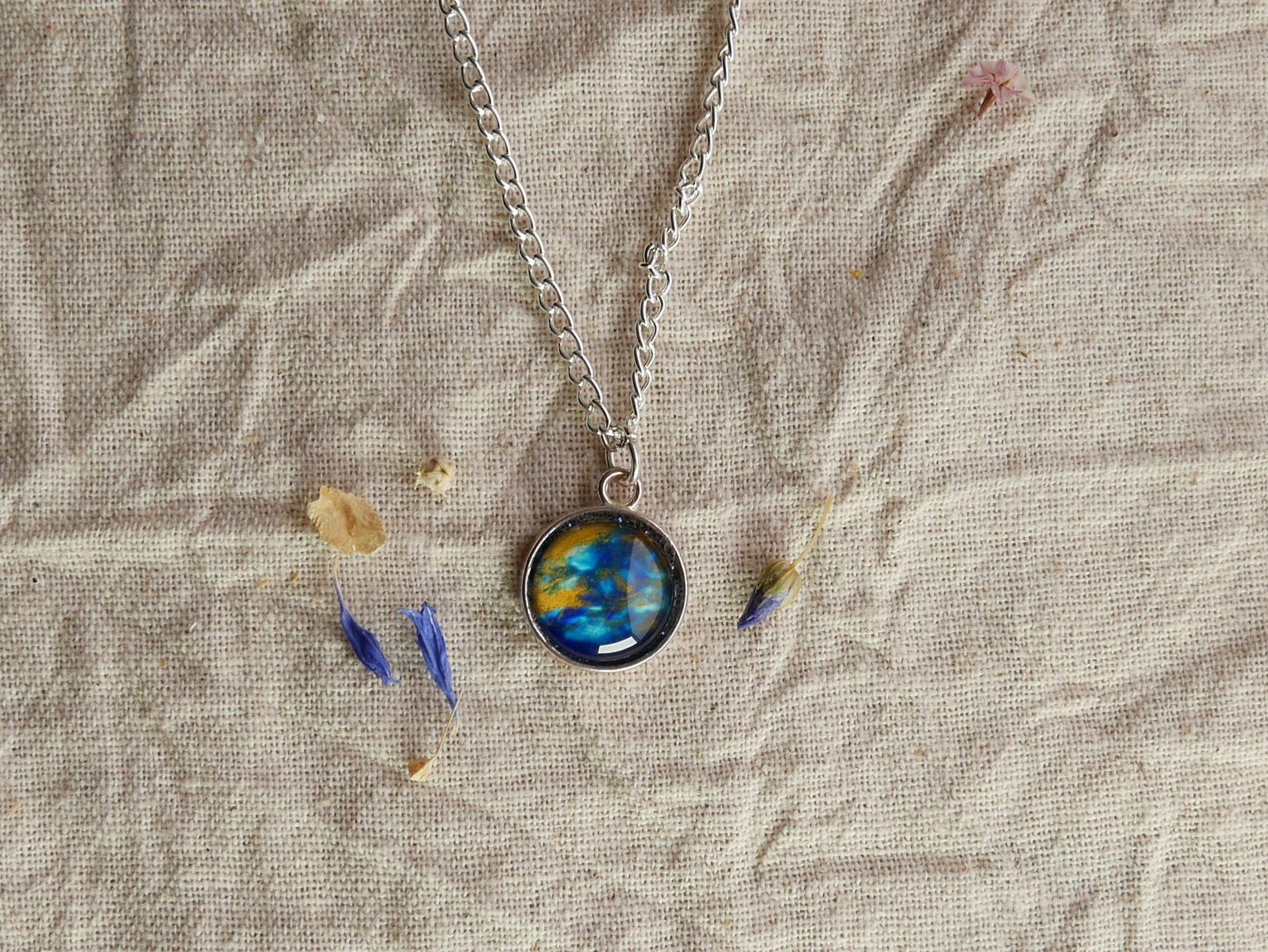 Silberne Halskette mit rundem Anhänger, darin eingefasst ein halbrunder Glasstein in blau, gold und glitzernd