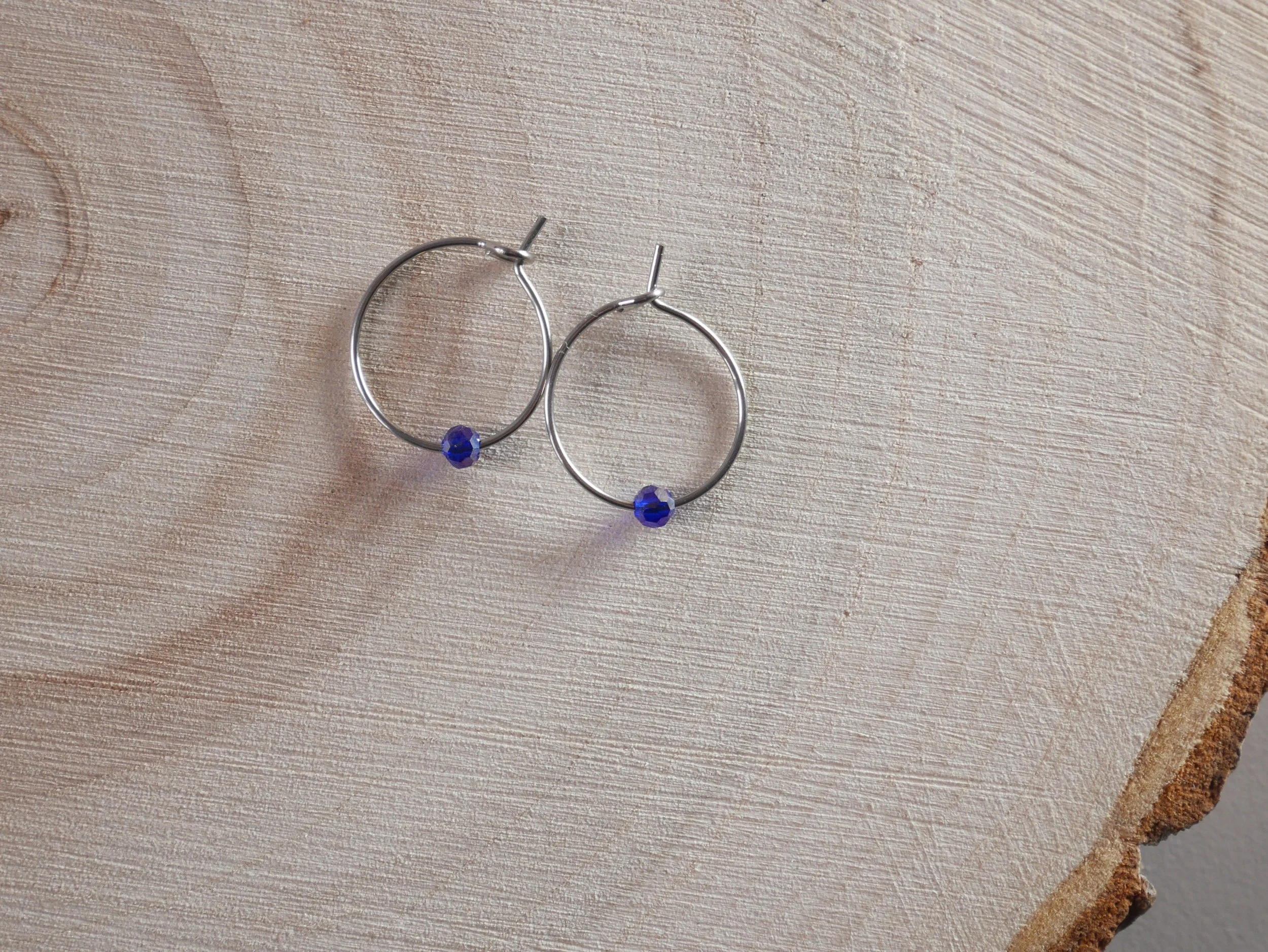 Kleine silberfarbene Creolen mit jeweils einer winzigen blauen Acrylperle