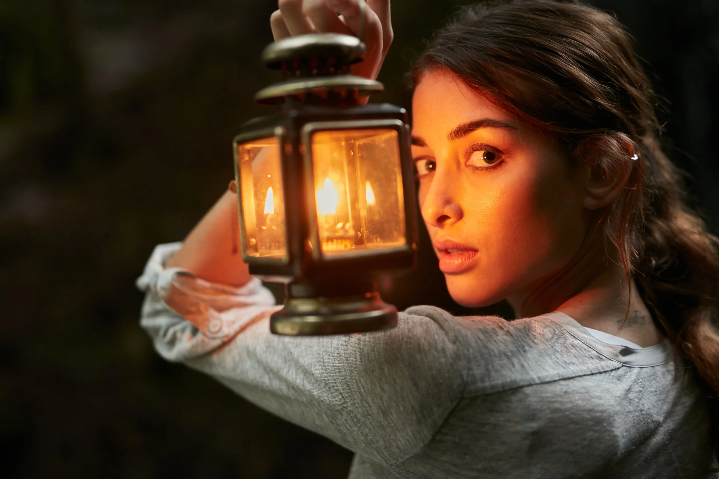 Woman holding a lantern in the dark, illuminating her face.