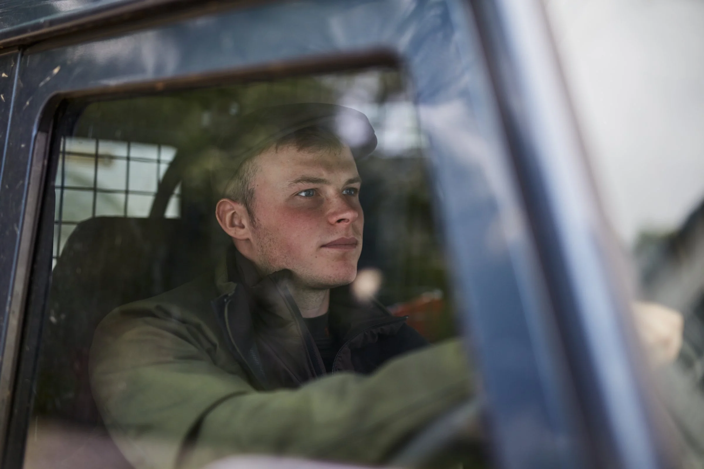 Young man wearing a cap driving a vehicle, seen through the window.