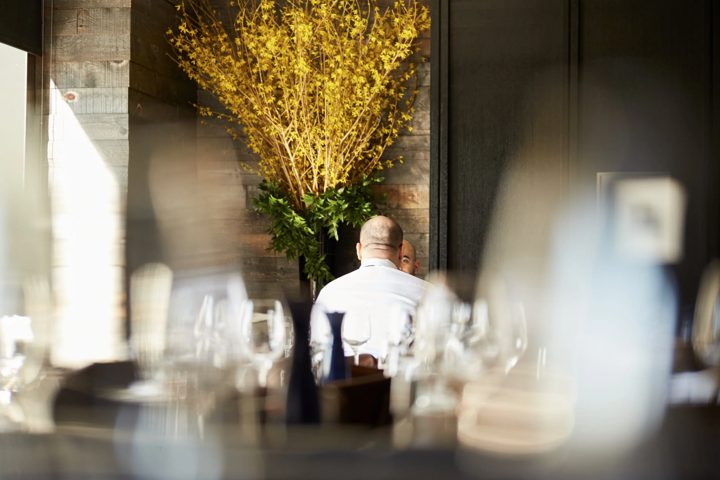 Blurred photo of two people in a restaurant with yellow flowers in the background.