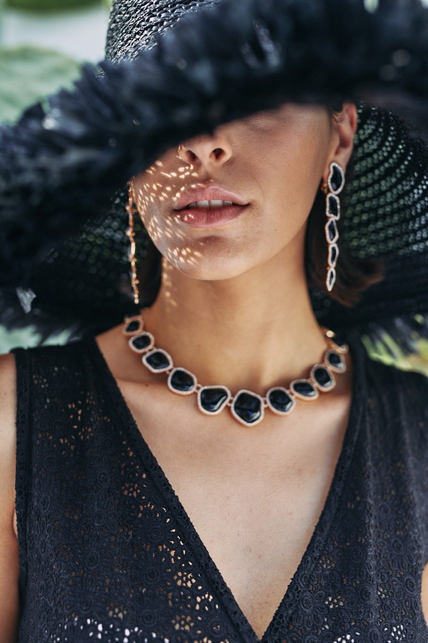 A woman wearing a large black hat, black earrings, and a black necklace, dressed in a black lace top.