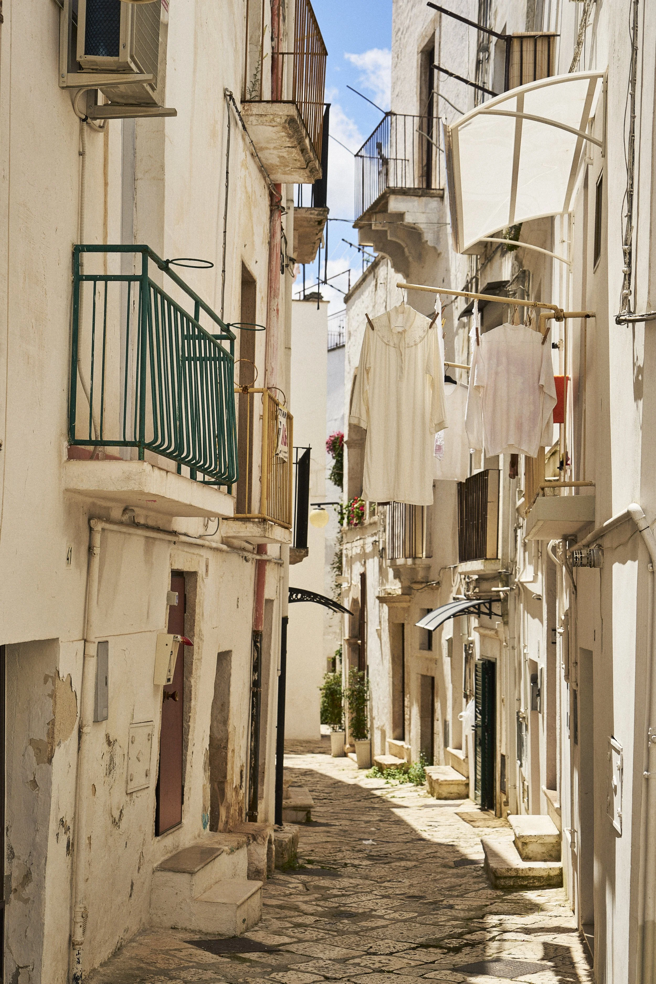 Narrow cobblestone alley with whitewashed buildings, balconies with clotheslines and drying laundry.