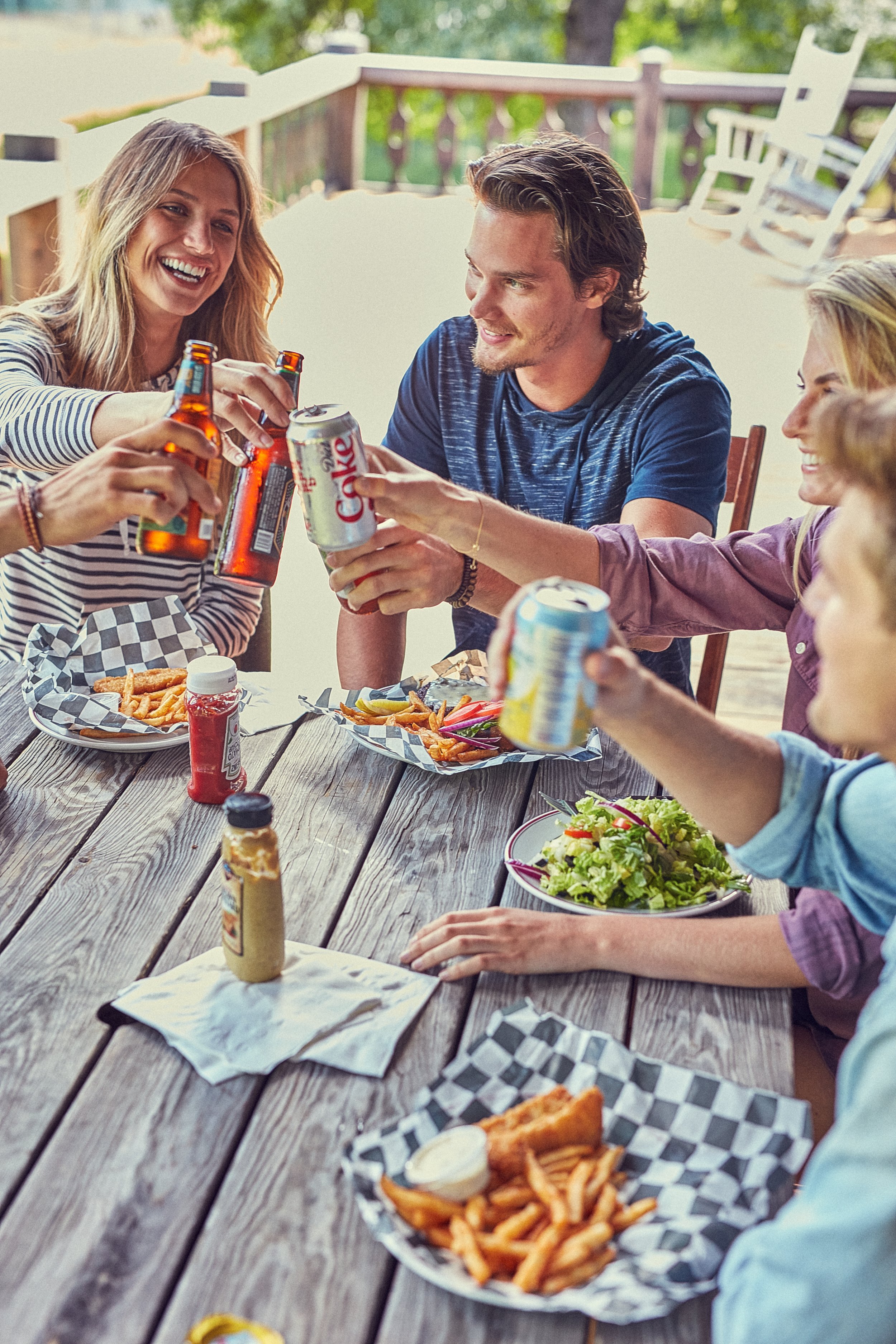 Group of friends toasting with drinks at outdoor picnic table with food, including fries and salad.
