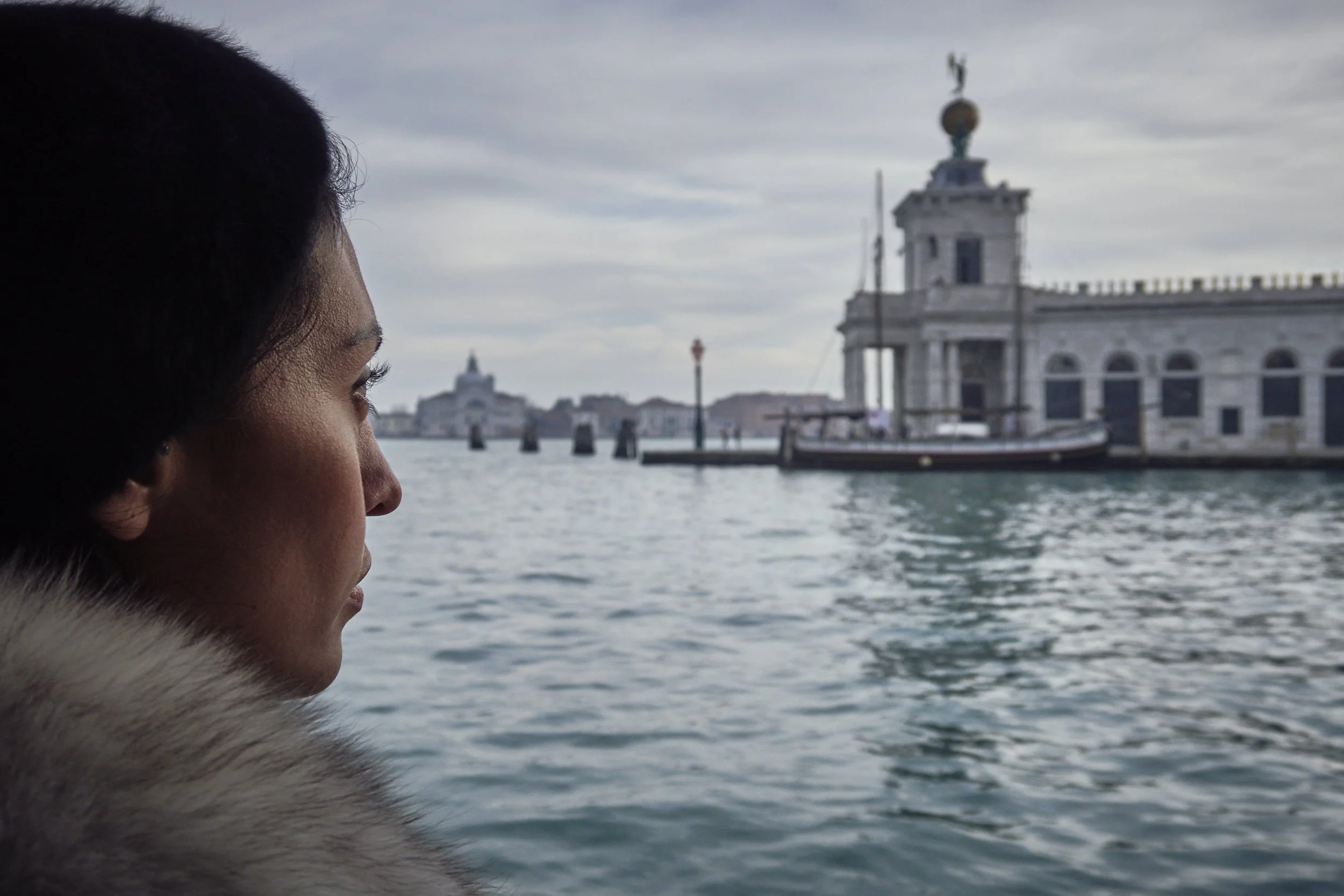 Person gazing over Venetian canal with historic building and sailboat