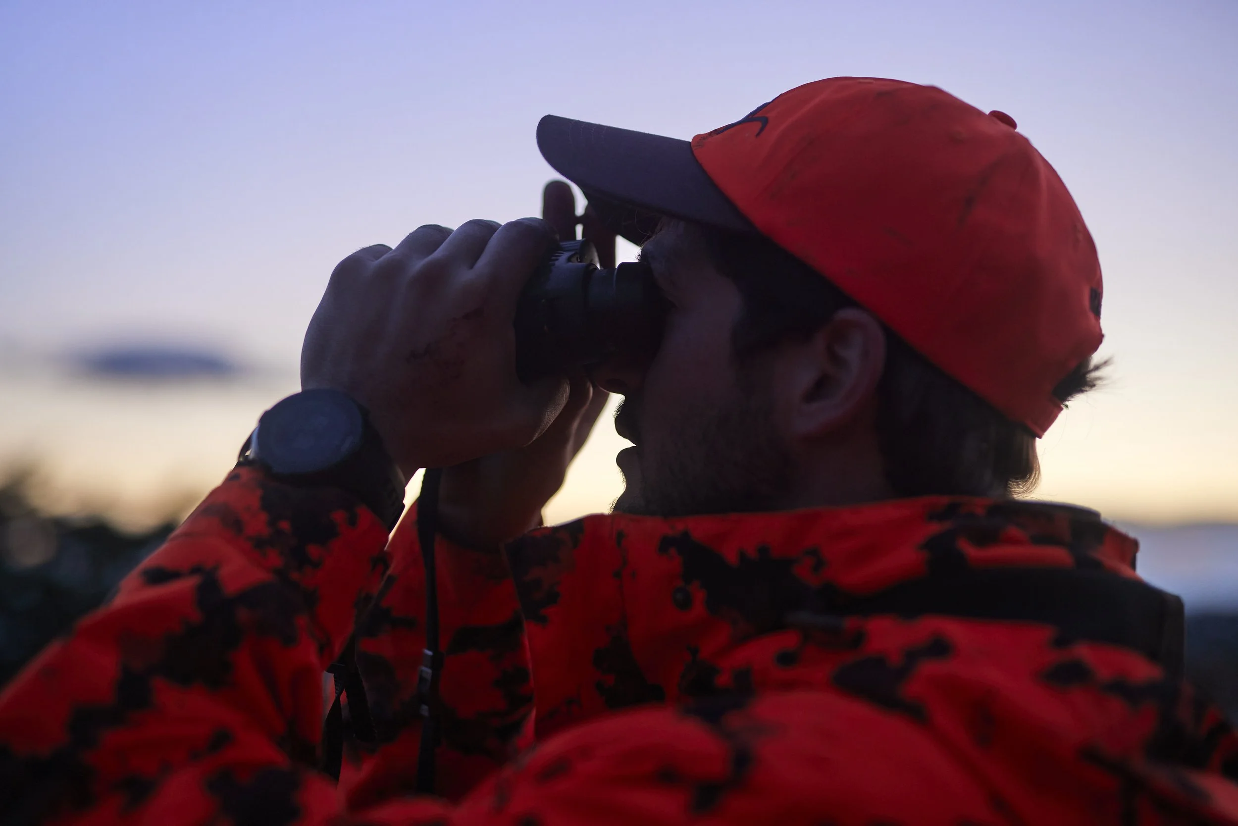 Man in orange camo holding binoculars at sunrise