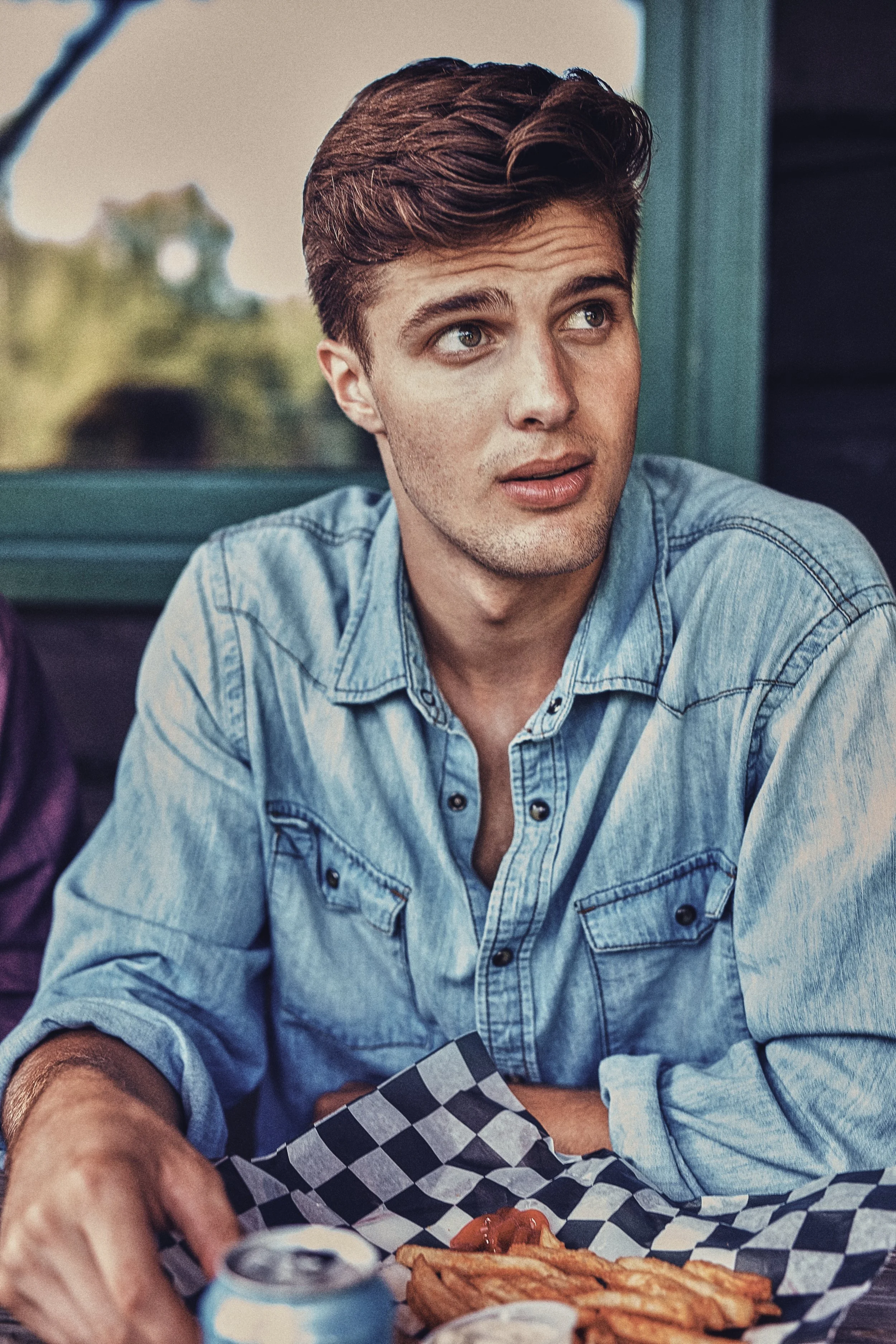 Man in denim shirt at a table with food and a drink