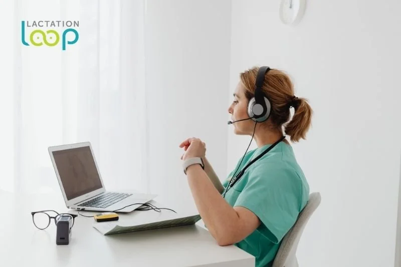 A lactation consultant wearing a headset sits at a desk with a laptop, ready to conduct a virtual consultation.