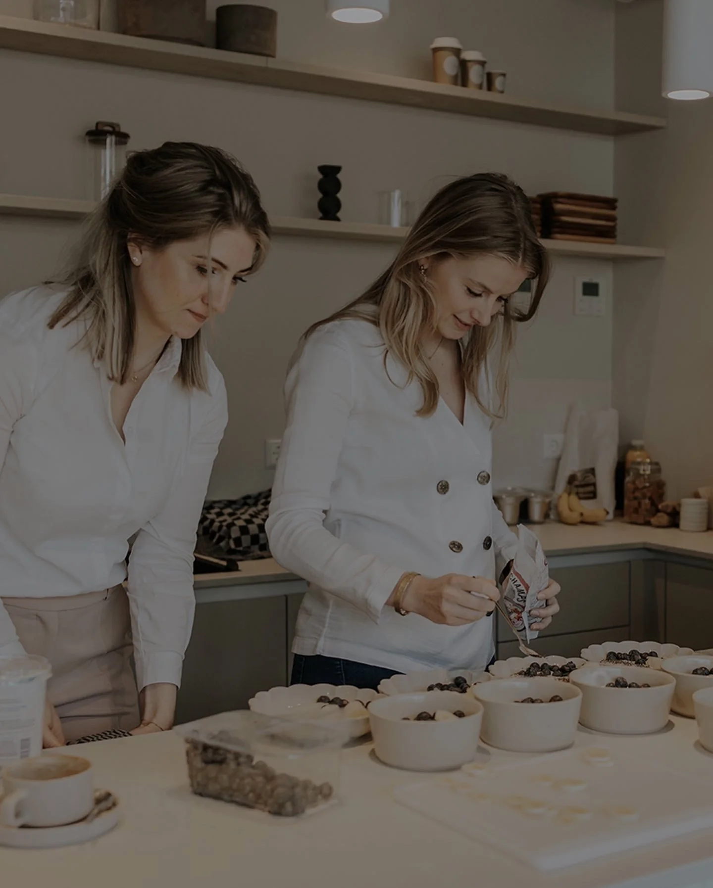 Twee vrouwen bereiden desserts met bosbessen in witte kommen op een keukenaanrecht.