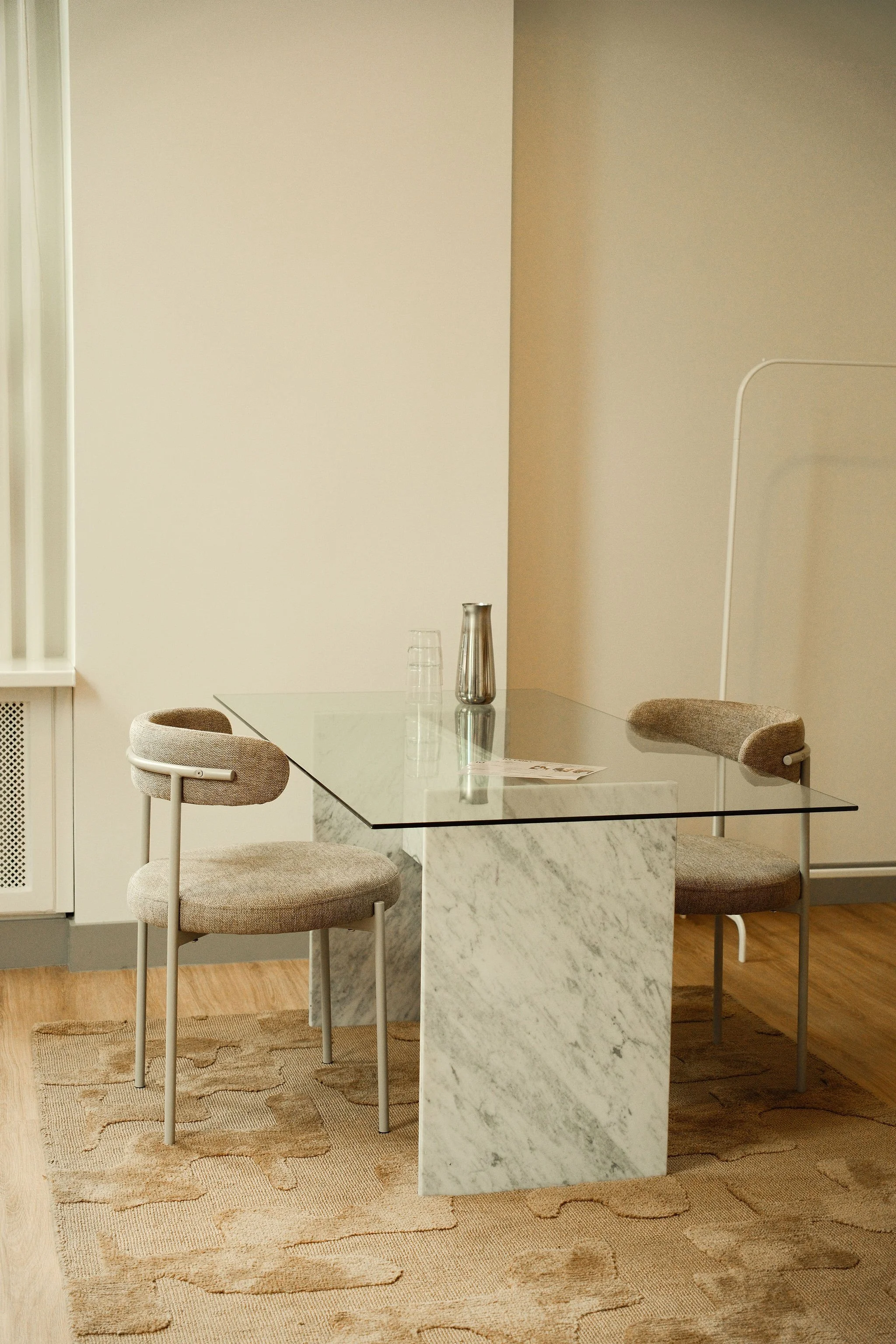 De afbeelding toont een wit betegeld en lichte muren in een elegante binnen gang met houten details en een trap met een tapijt. Er zijn glazen deuren en een deur met gouden handvatten aan de linkerkant. Ruimte bij Ivy Office.