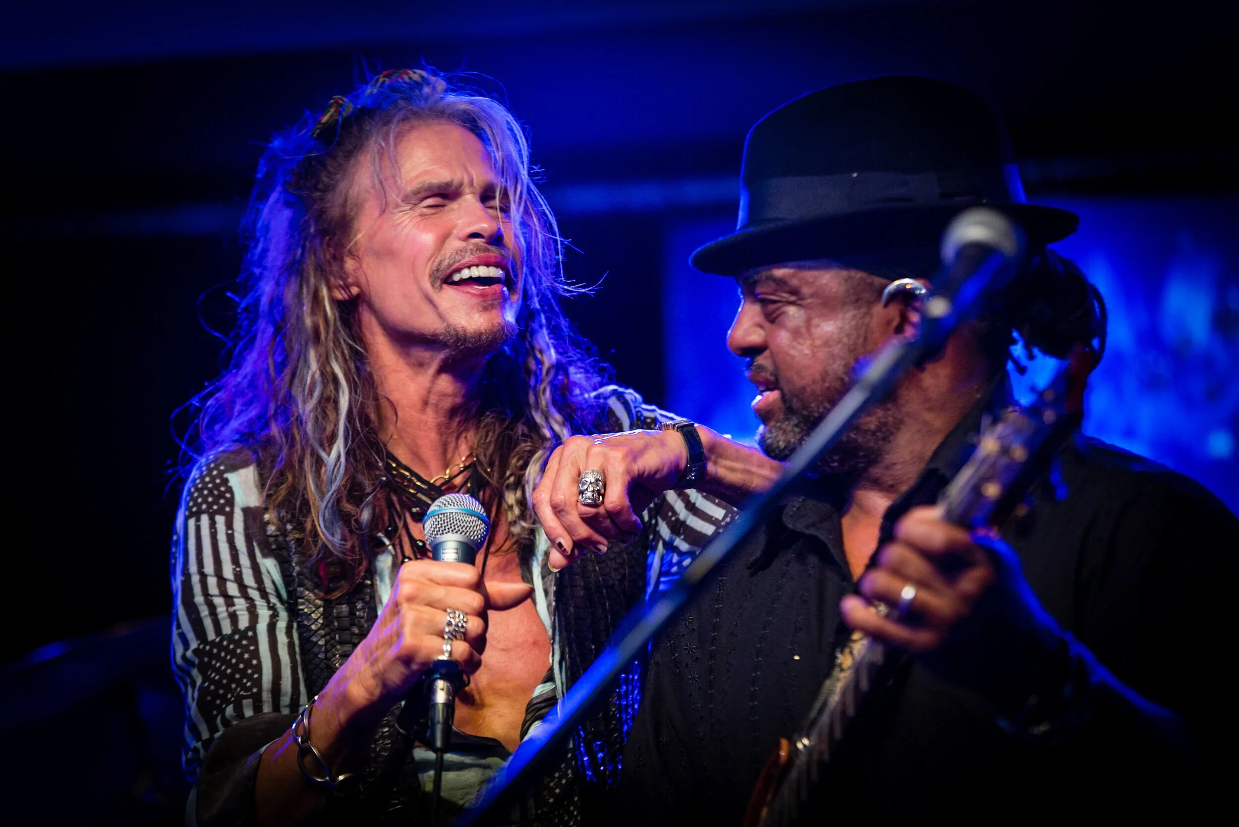 Two musicians performing on stage with one holding a microphone and the other playing a stringed instrument.