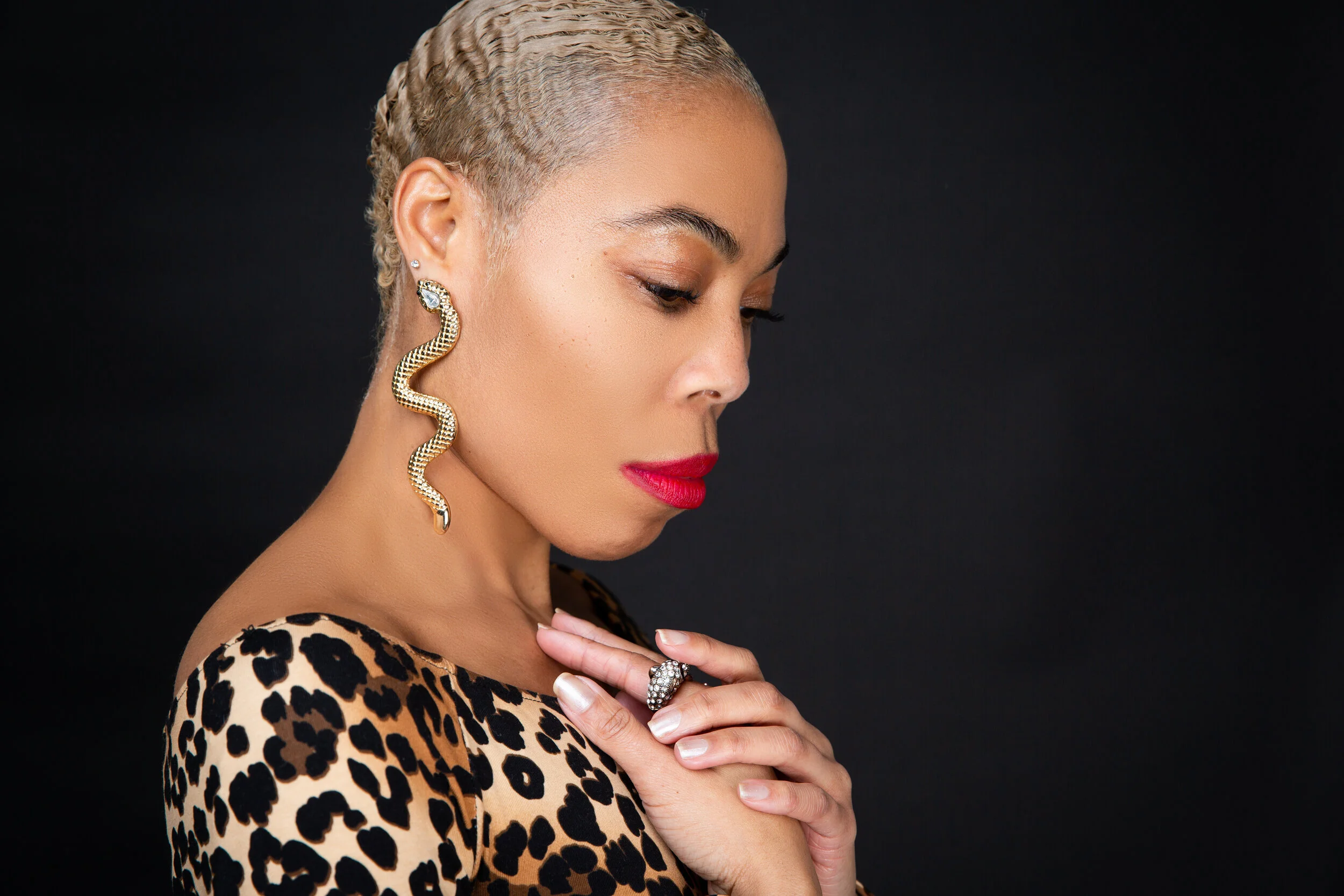Woman with gold snake-shaped earring and leopard print top, side profile.