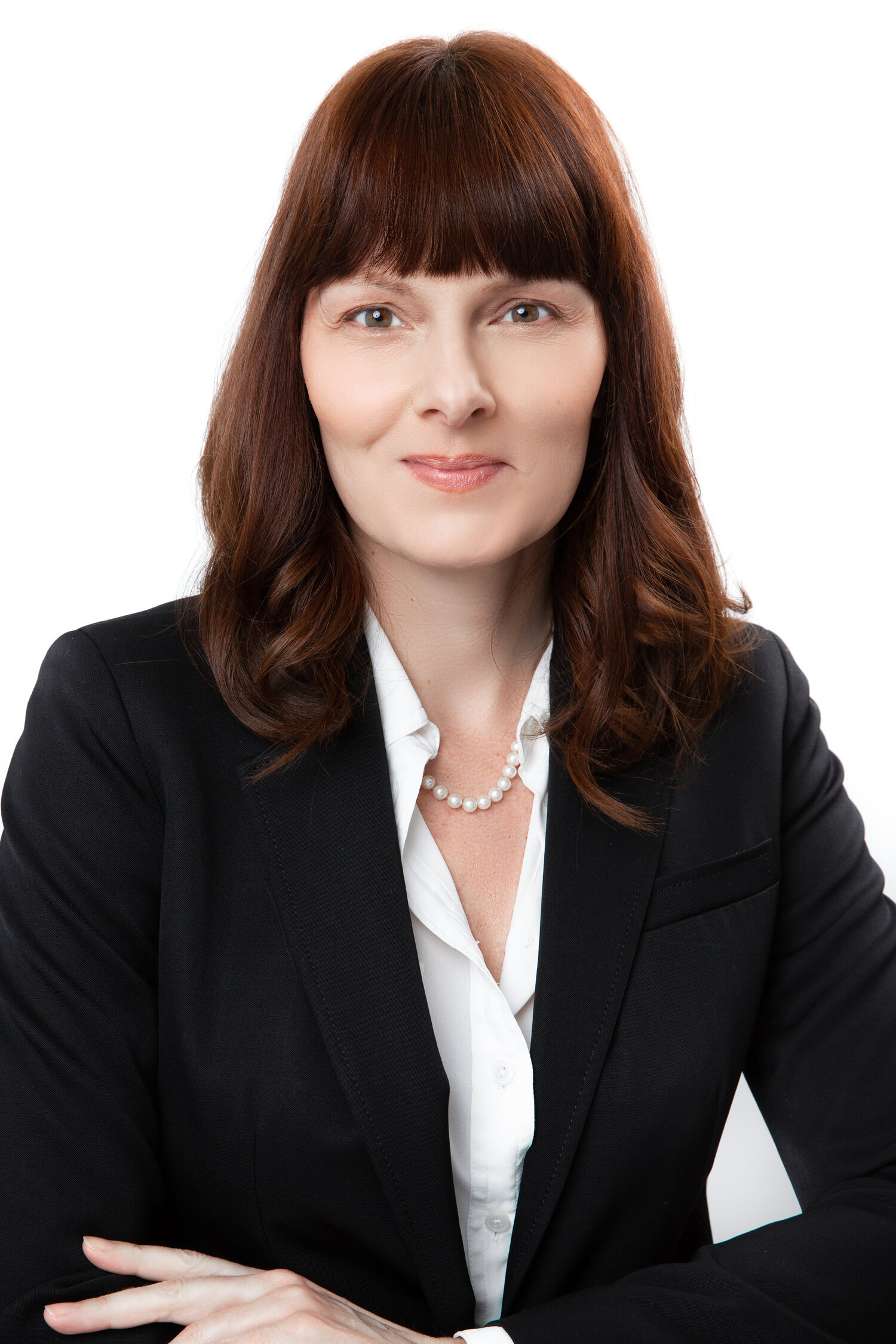 Portrait of a woman in a black blazer and white shirt, wearing a pearl necklace, against a white background.