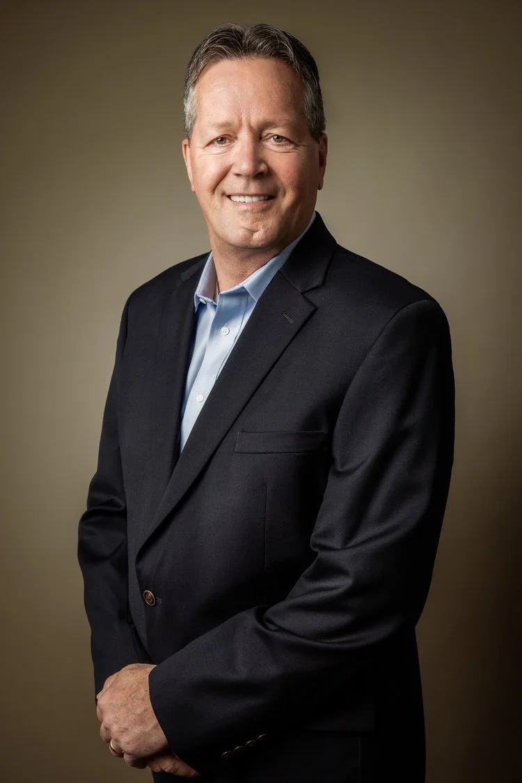 Smiling man in a suit posing for a portrait against a neutral background.