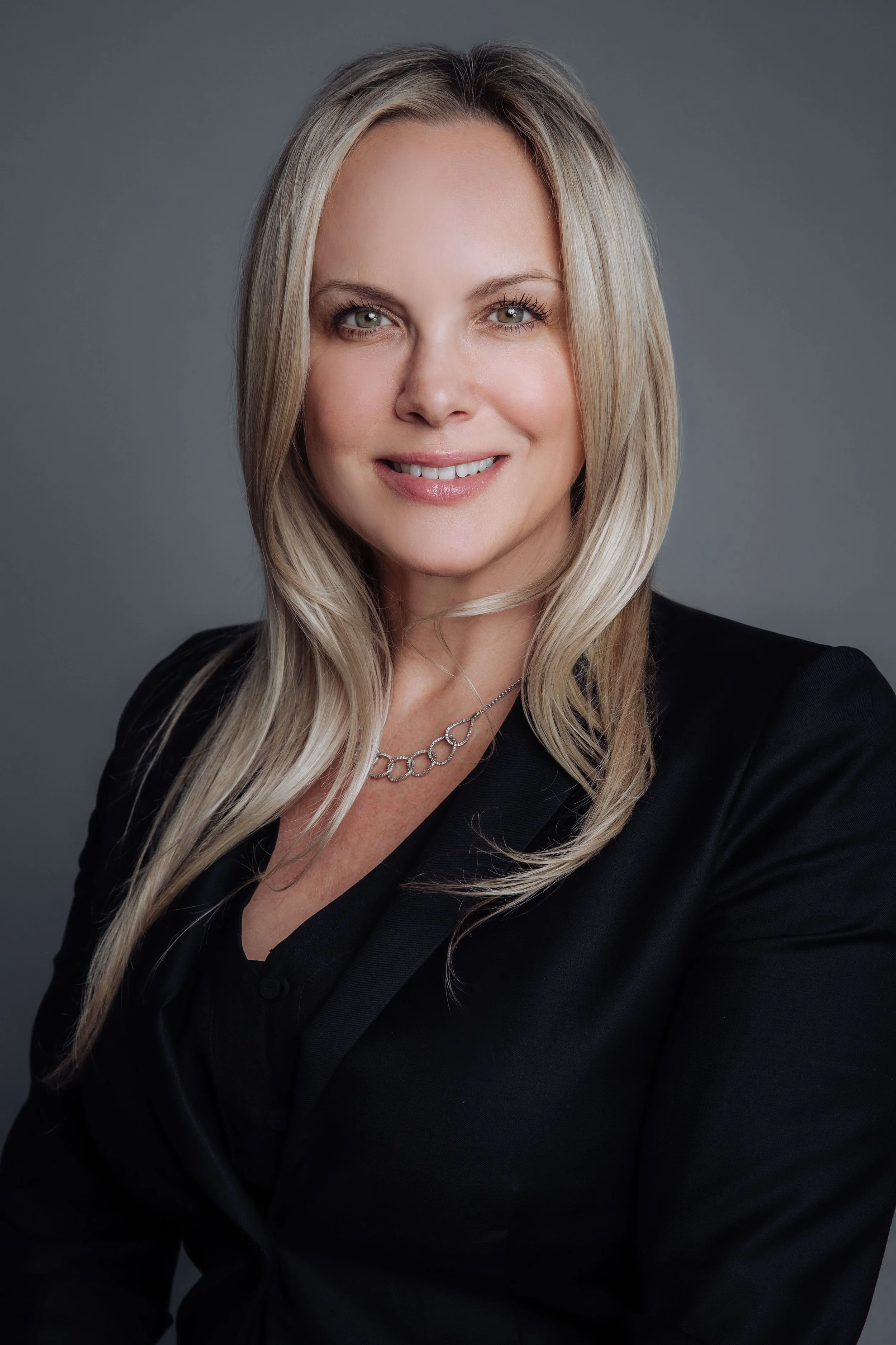 Smiling woman with long blonde hair wearing a black blazer and silver necklace