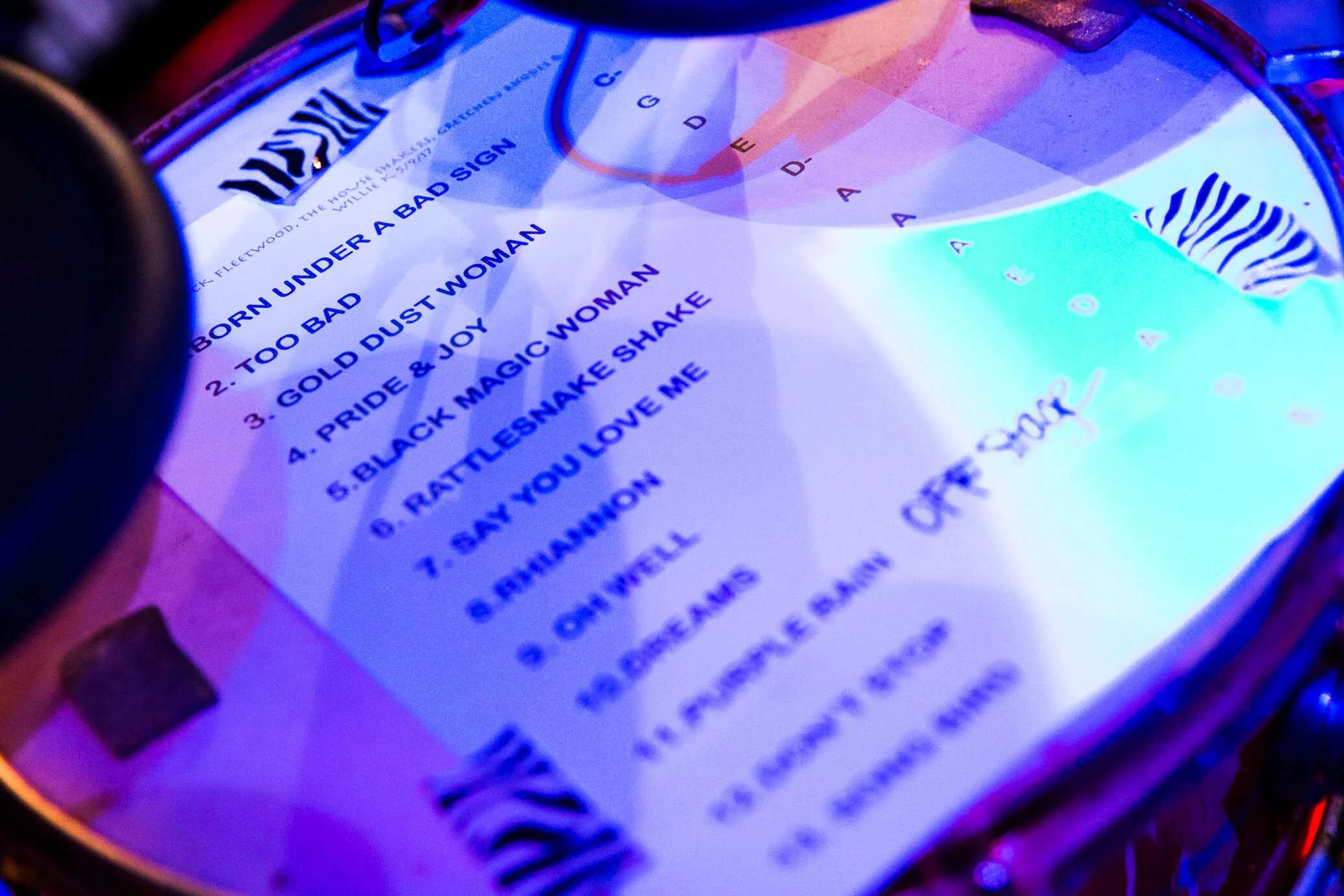 Close-up of a band's setlist on a drum, featuring song titles and a zebra print logo, under blue lighting.