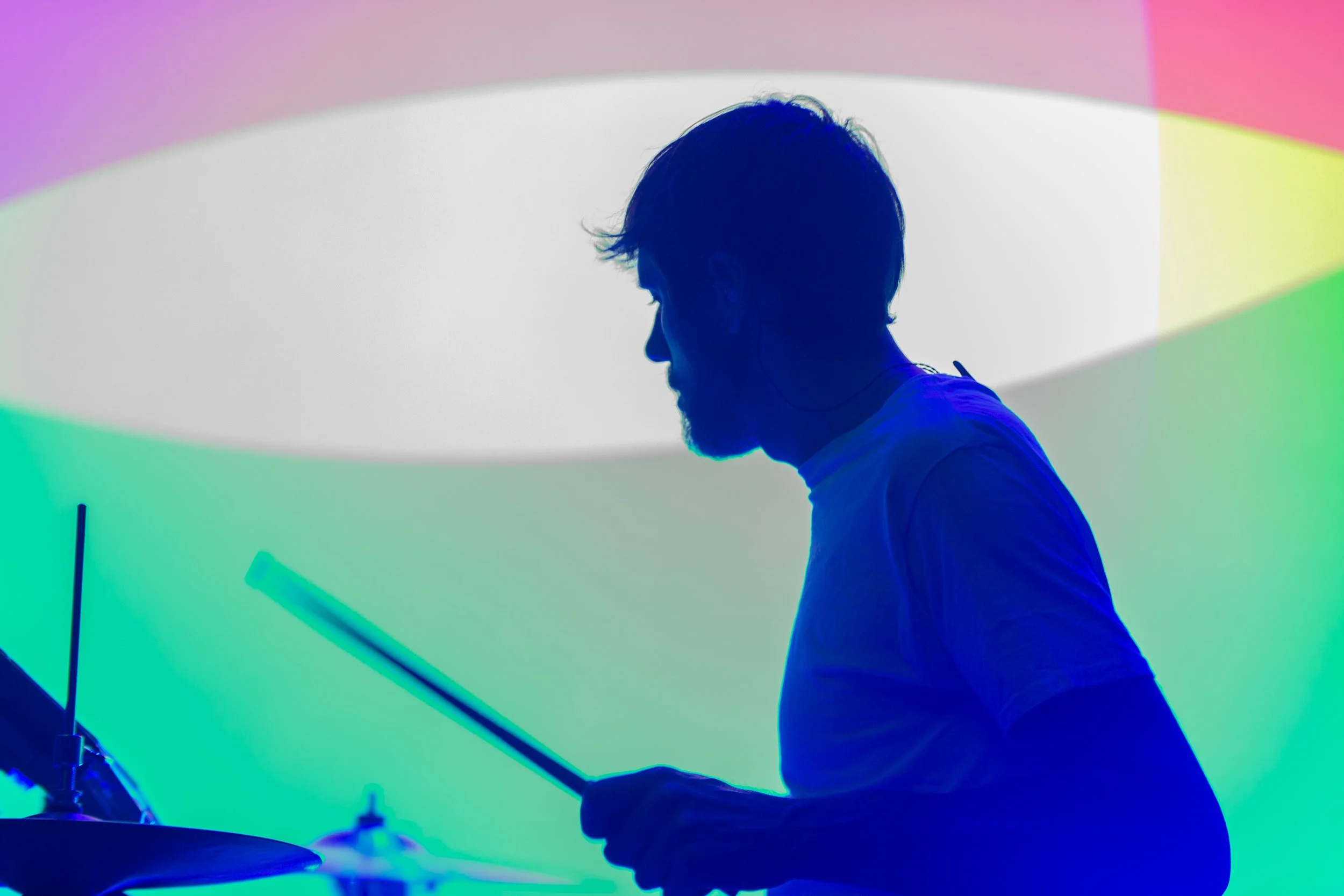 Silhouette of a drummer playing drums under colorful stage lights.