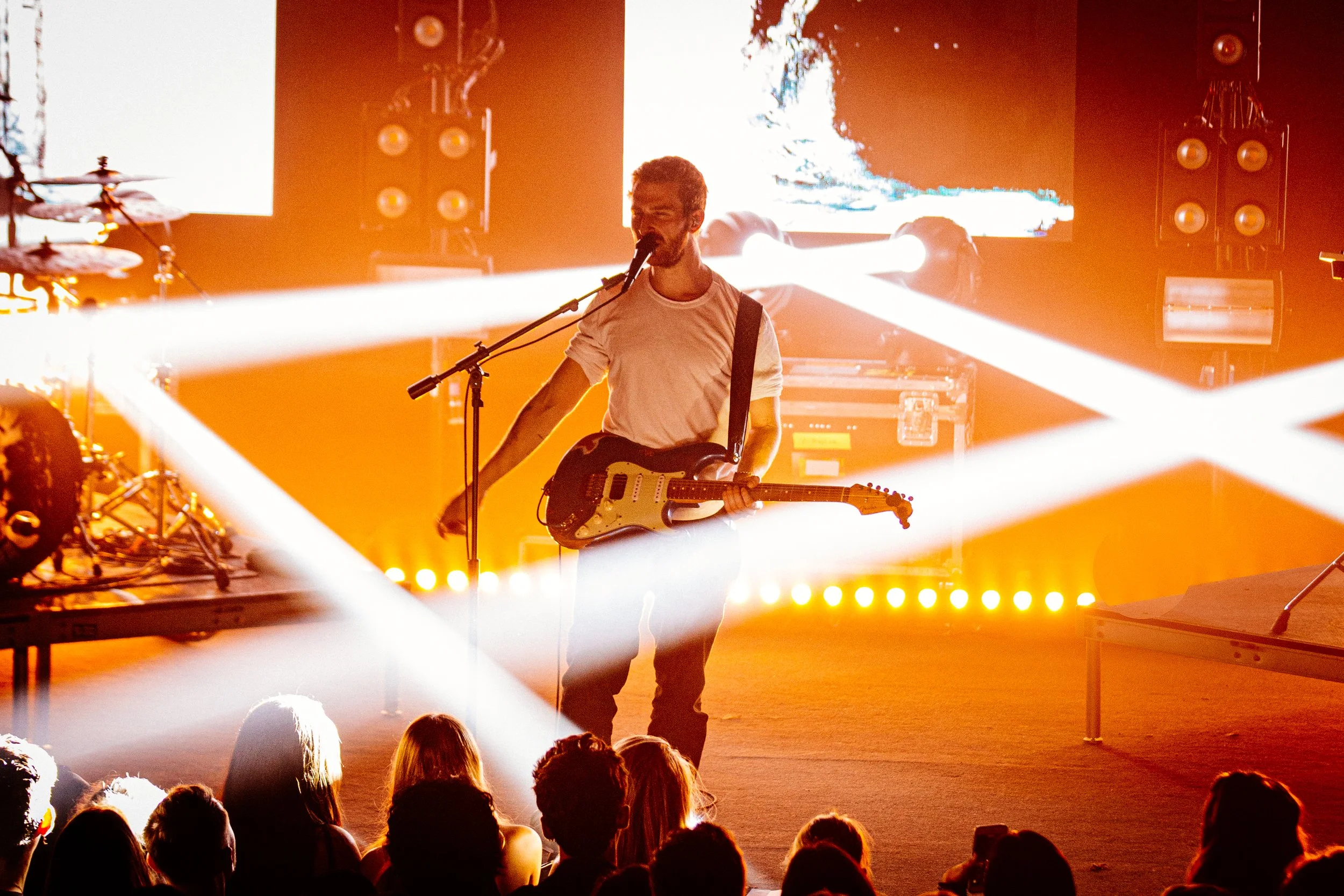 Musician on stage with guitar and microphone, vibrant lighting, audience in foreground.