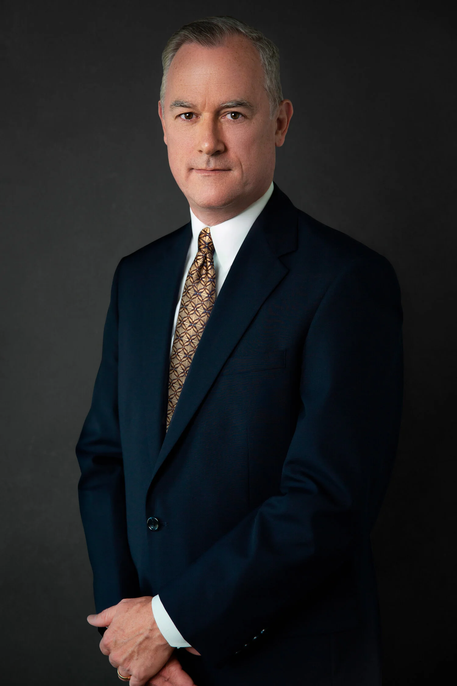 Man in a suit with geometric patterned tie against a dark background