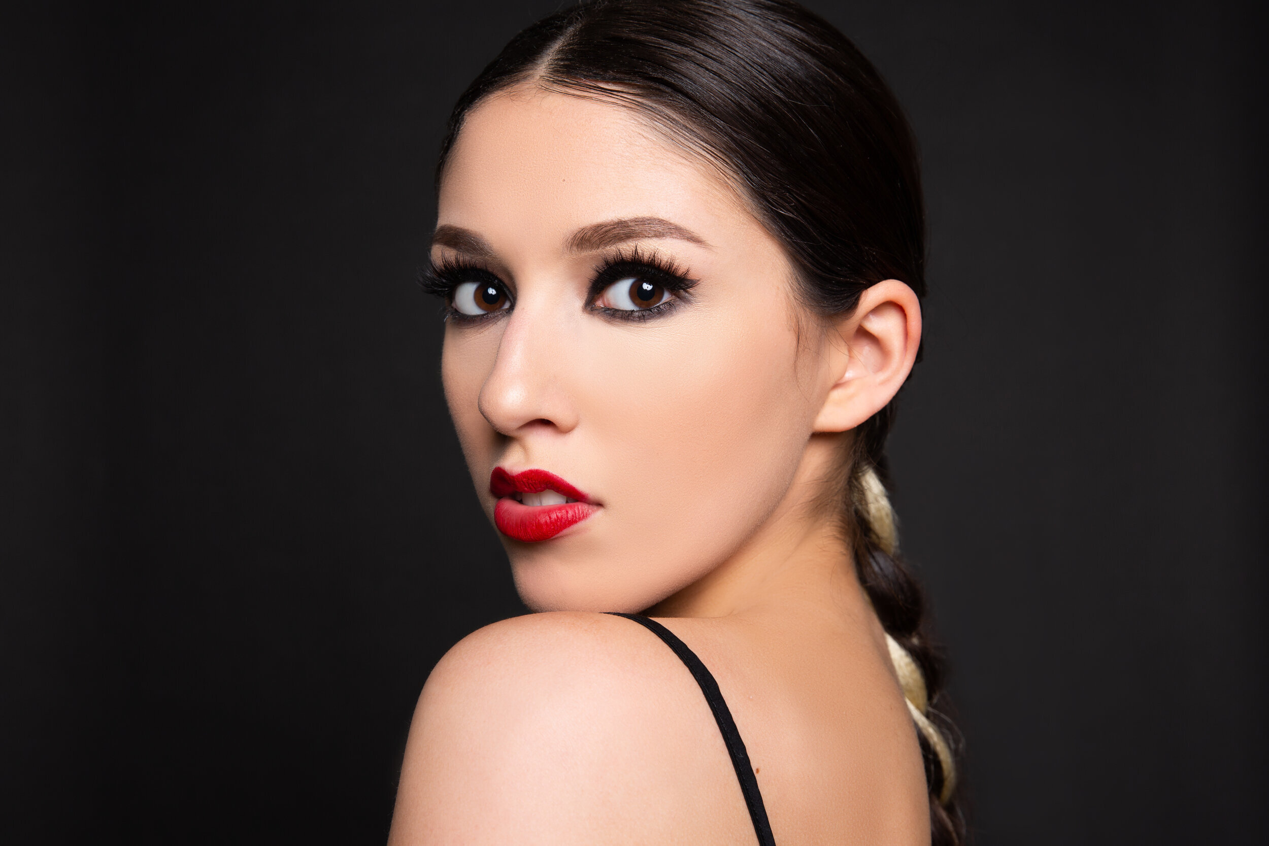 Portrait of a woman with dark hair, braided, and wearing red lipstick on a black background.