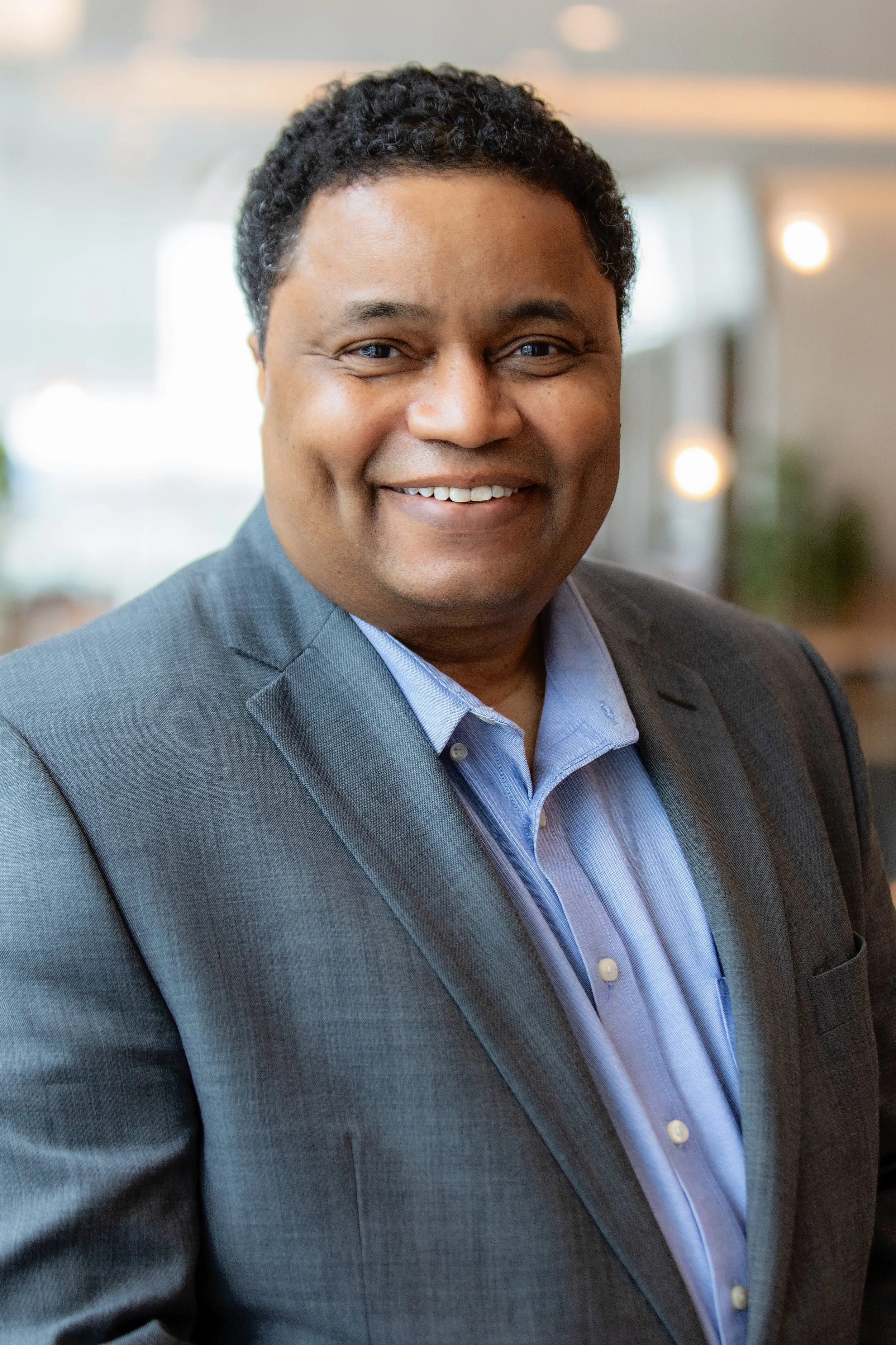 A man in a gray suit and blue shirt smiling.