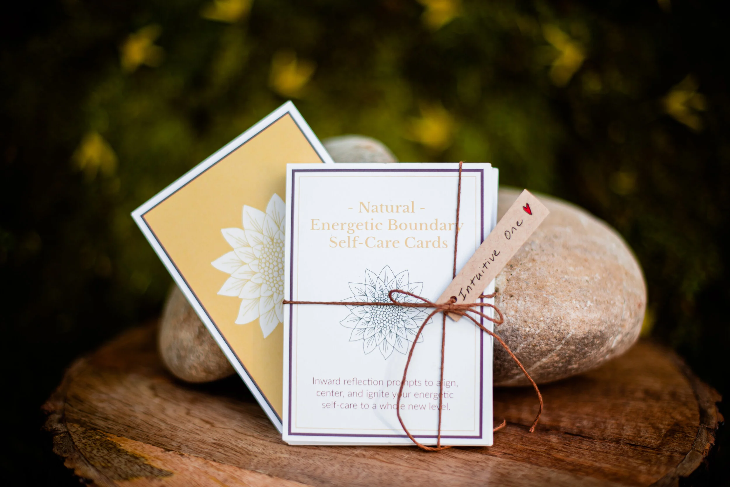 Photo of the "Natural Energetic Boundary Cards: tied up with twine with a gift tag that reads, "Intuitive One" resting on a rock with a mossy background