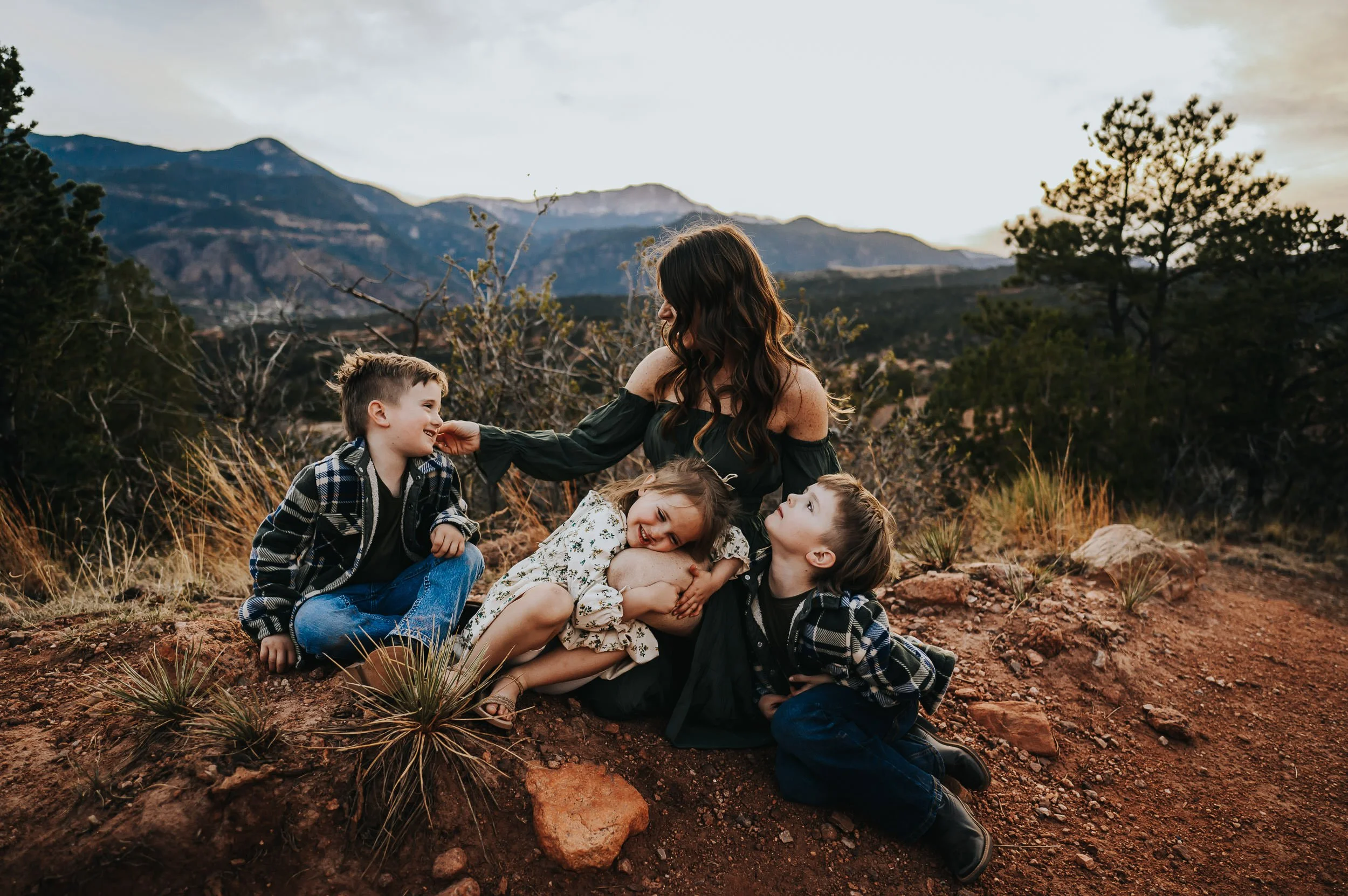 Family of four sitting together on red sandstone, red rock formations behind them.