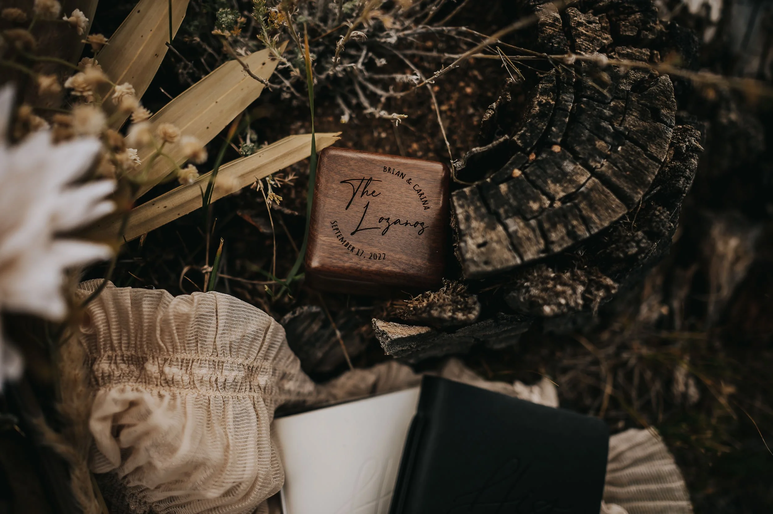 A wedding detail flatlay with a vow book, dried botanicals, wooden elements, and soft textures.