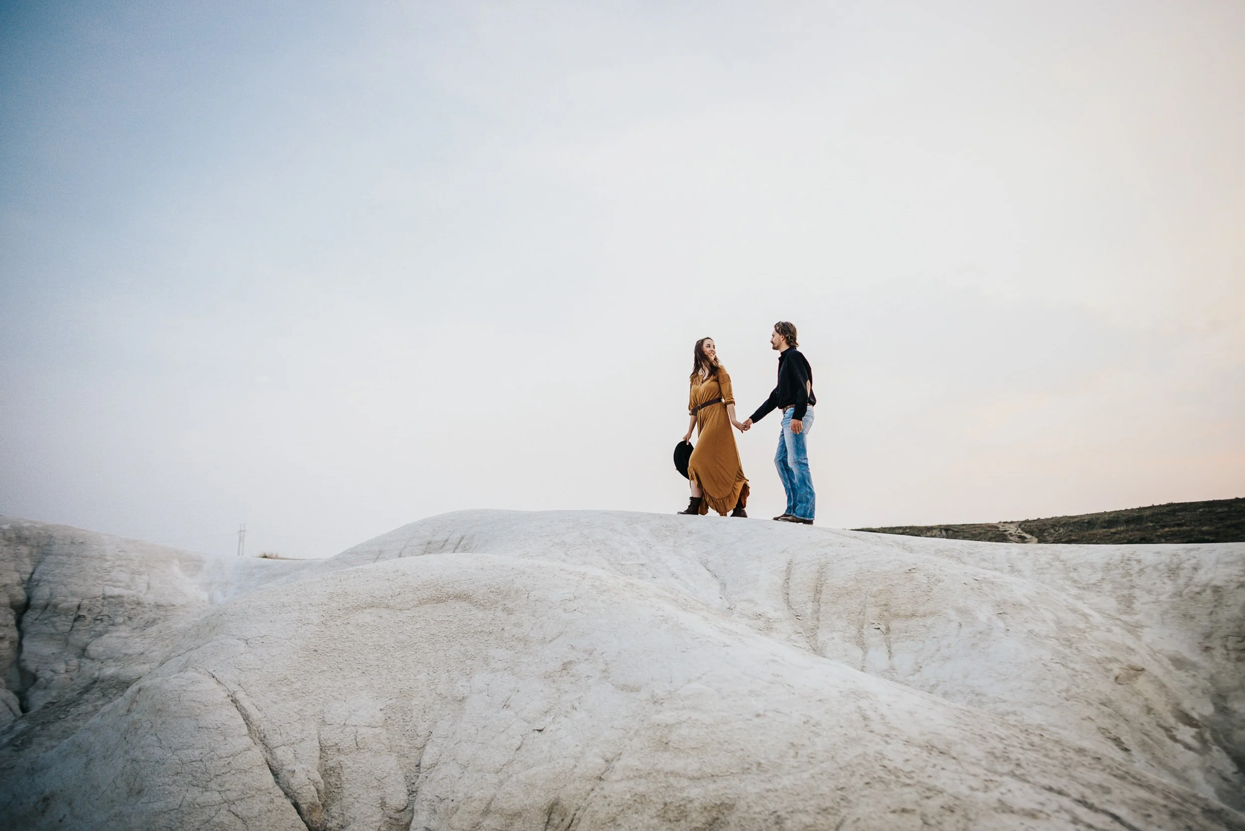 A couples stands close together at Paint Mines Park, wide shot with open sky.