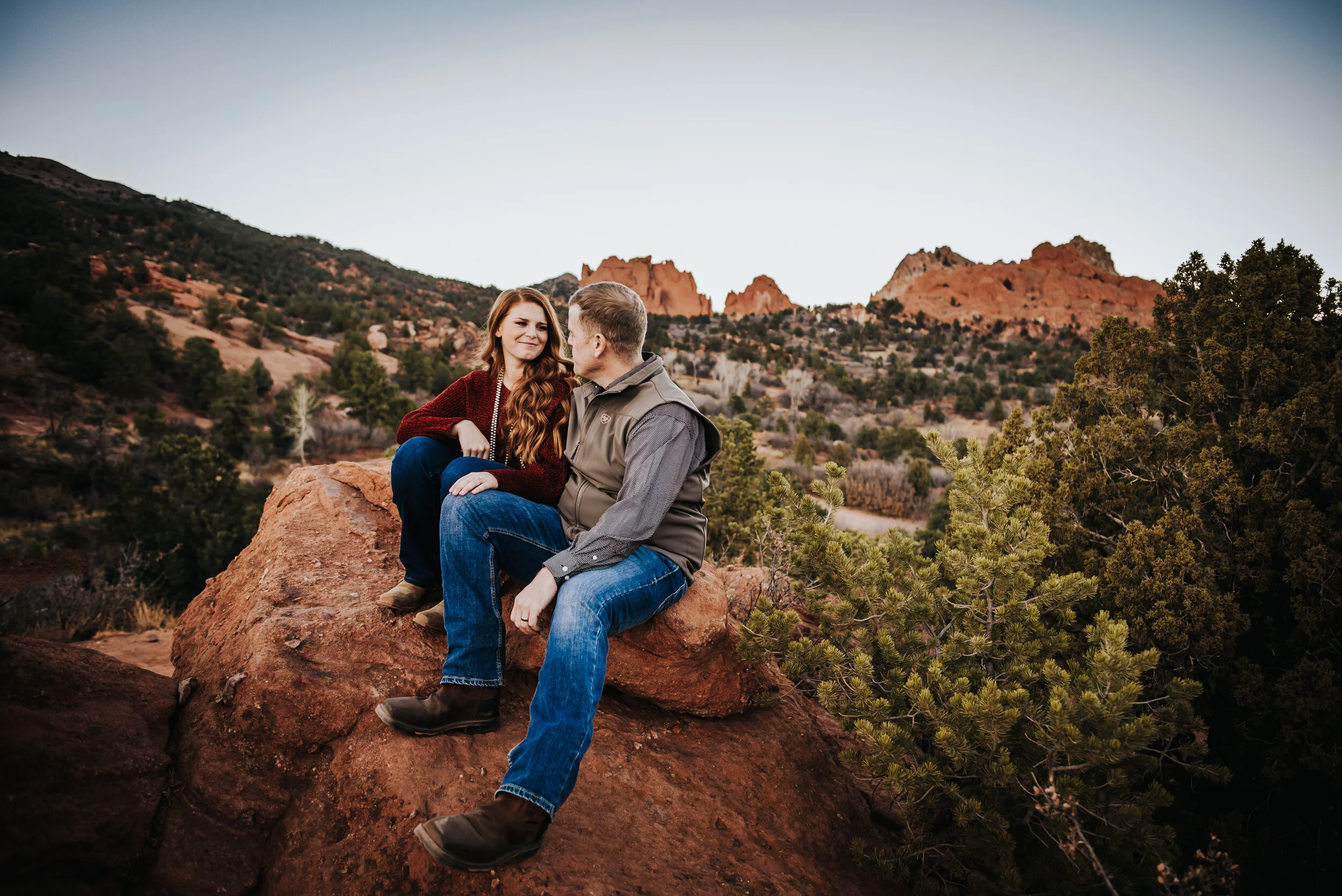 Couple sitting together on red rock formations at golden hour.