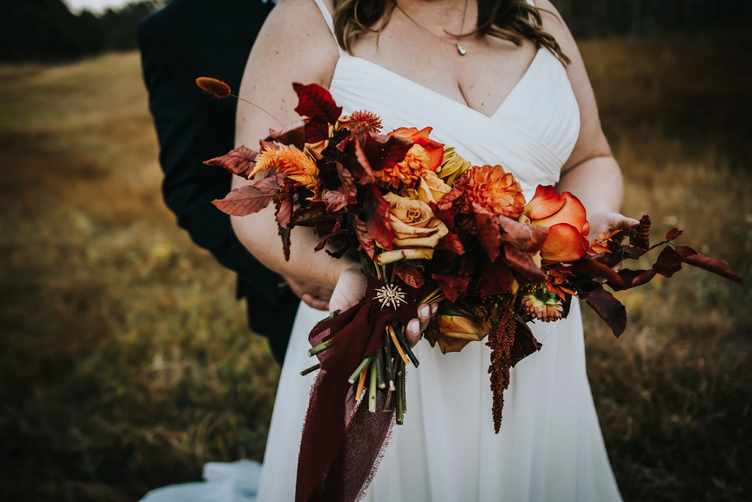 Bride holding a rich autumn bouquet of orange and burgundy flowers at a Black Forest Colorado backyard wedding.