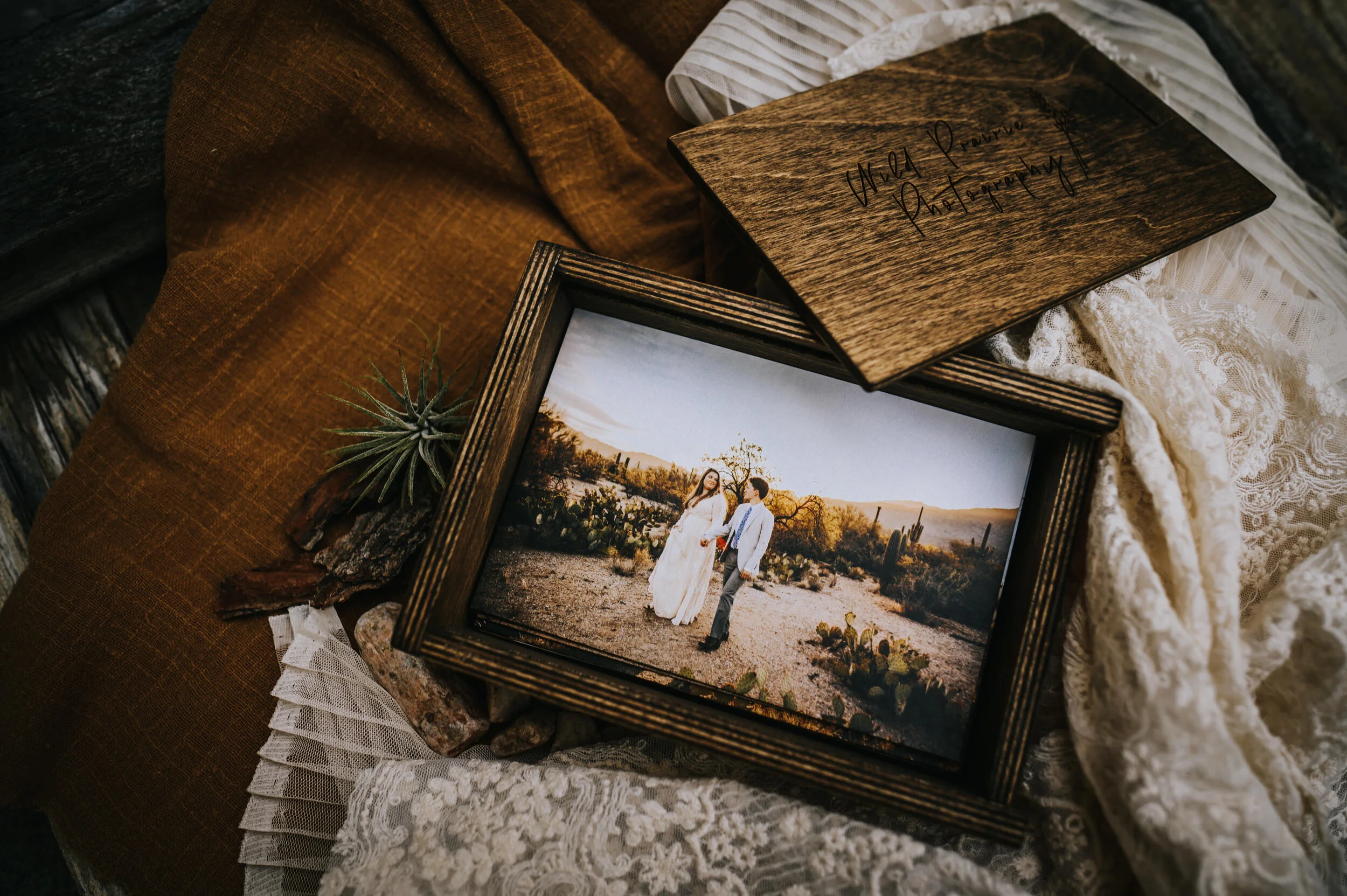 Open wooden box displaying a framed elopement portrait on linen.