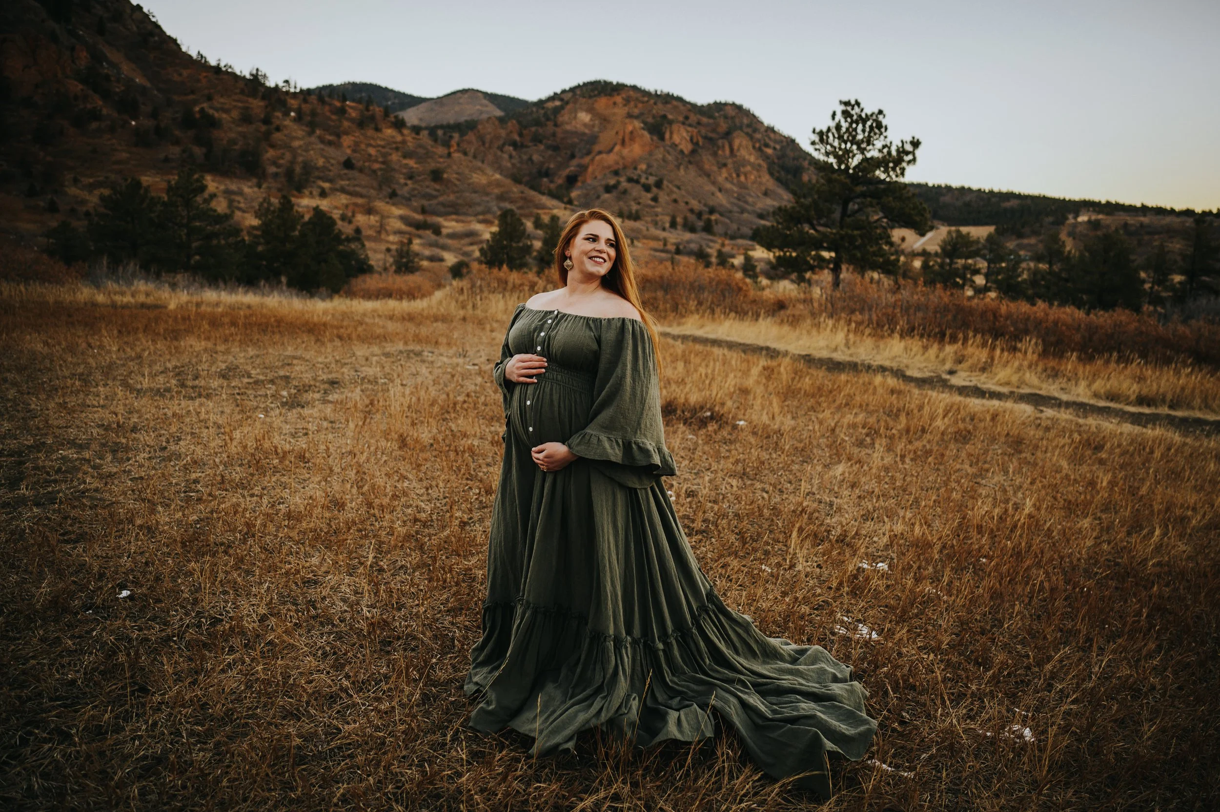 Pregnant woman in flowing dress with mountains behind her during a Cheyenne Canon maternity session.