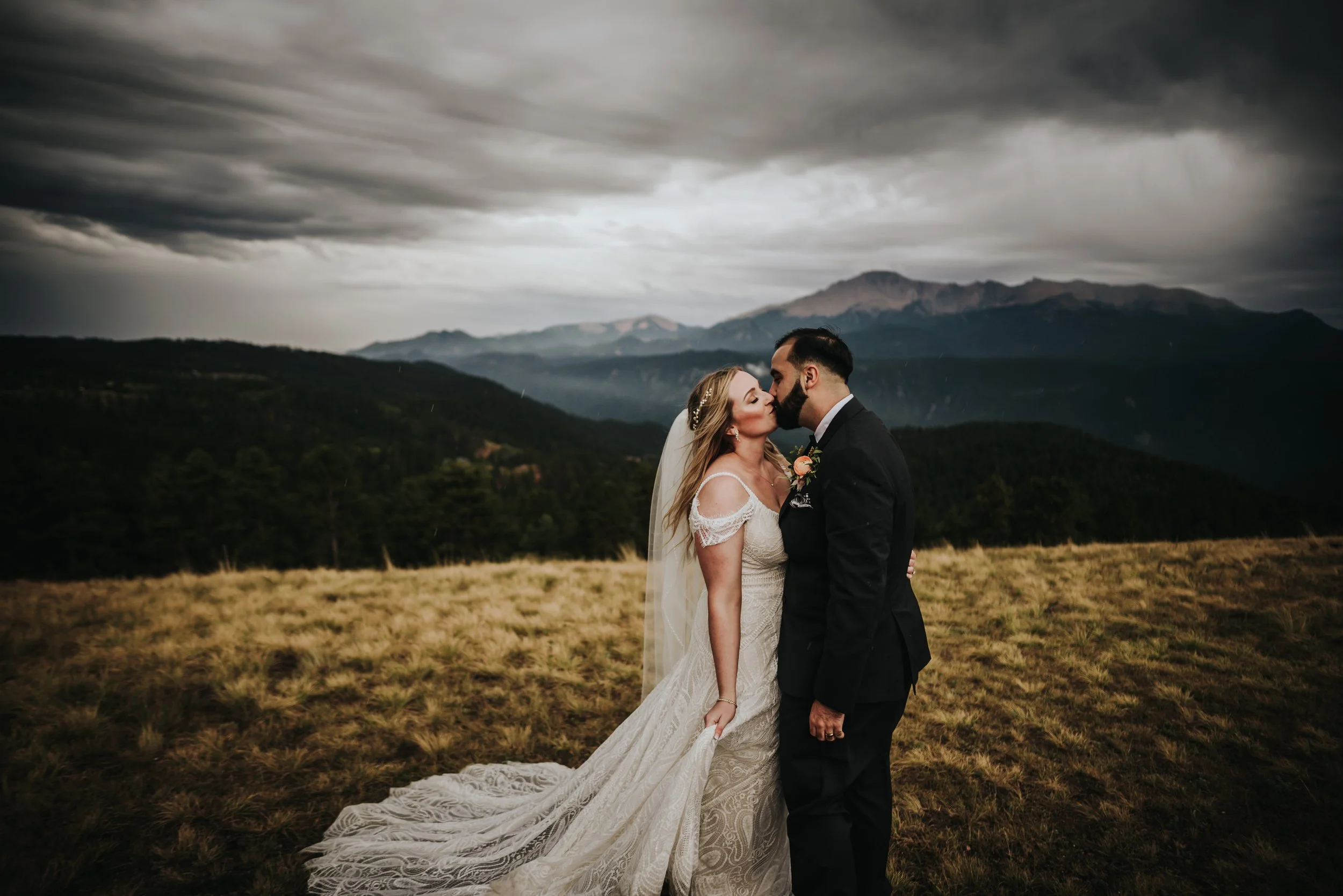 Bride and groom embracing on a mountain ridge under a dramatic cloudy sky at the Edgewood Inn in Woodland Park Colorado.