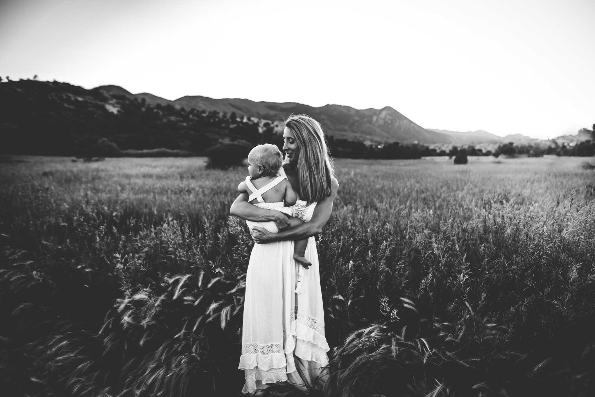 A mother wearing a white lace dress holds her young song tightly and sways in the tall grass at Ute Valley Park.