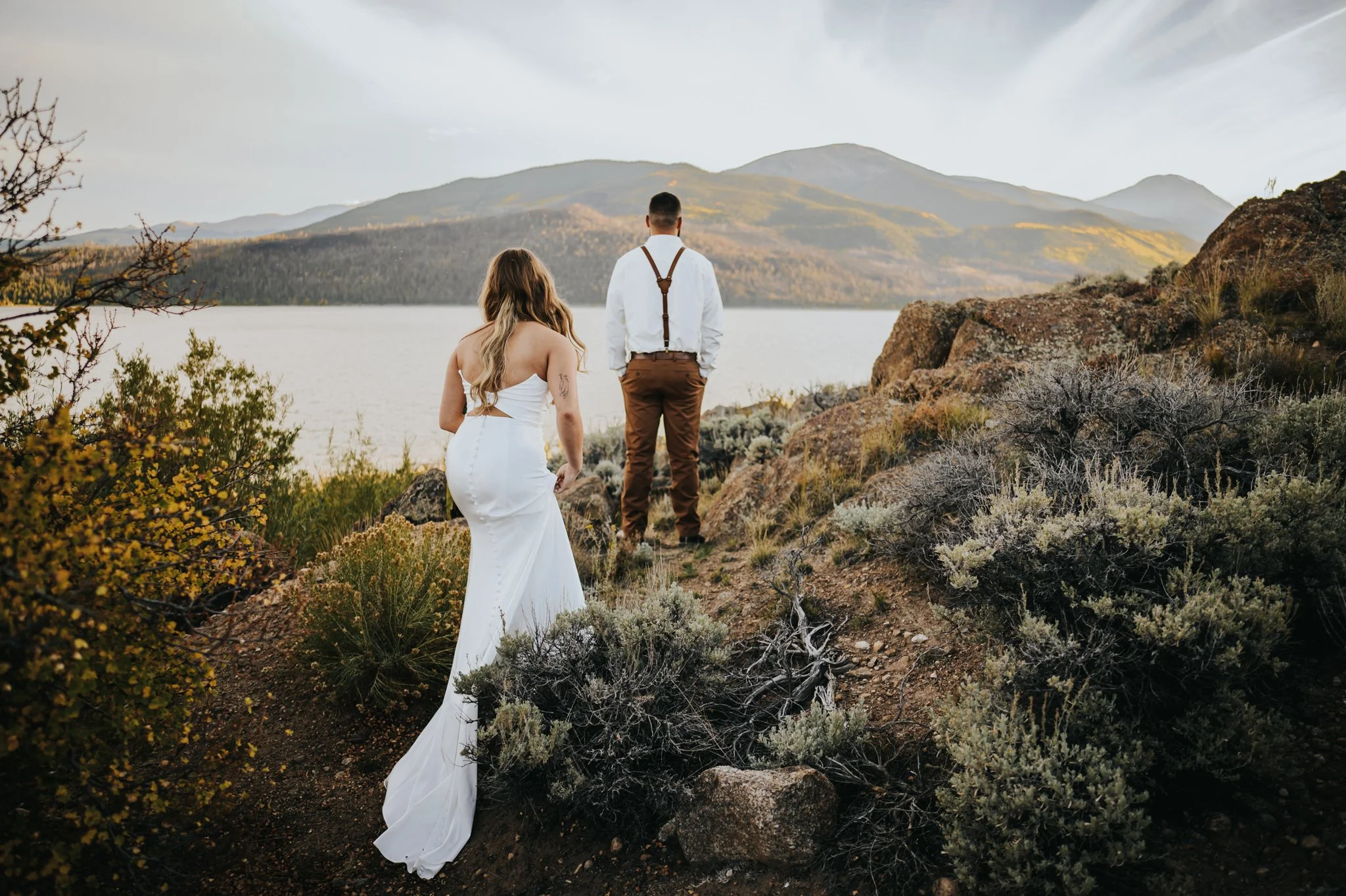 Couple walking toward Twin Lakes, bride's white gown trailing behind her with mountains in the distance.