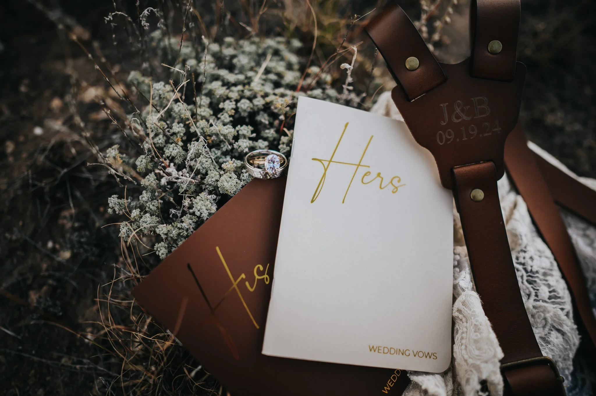 Wedding vow books and a leather journal with delicate wildflowers in a styled flat lay.