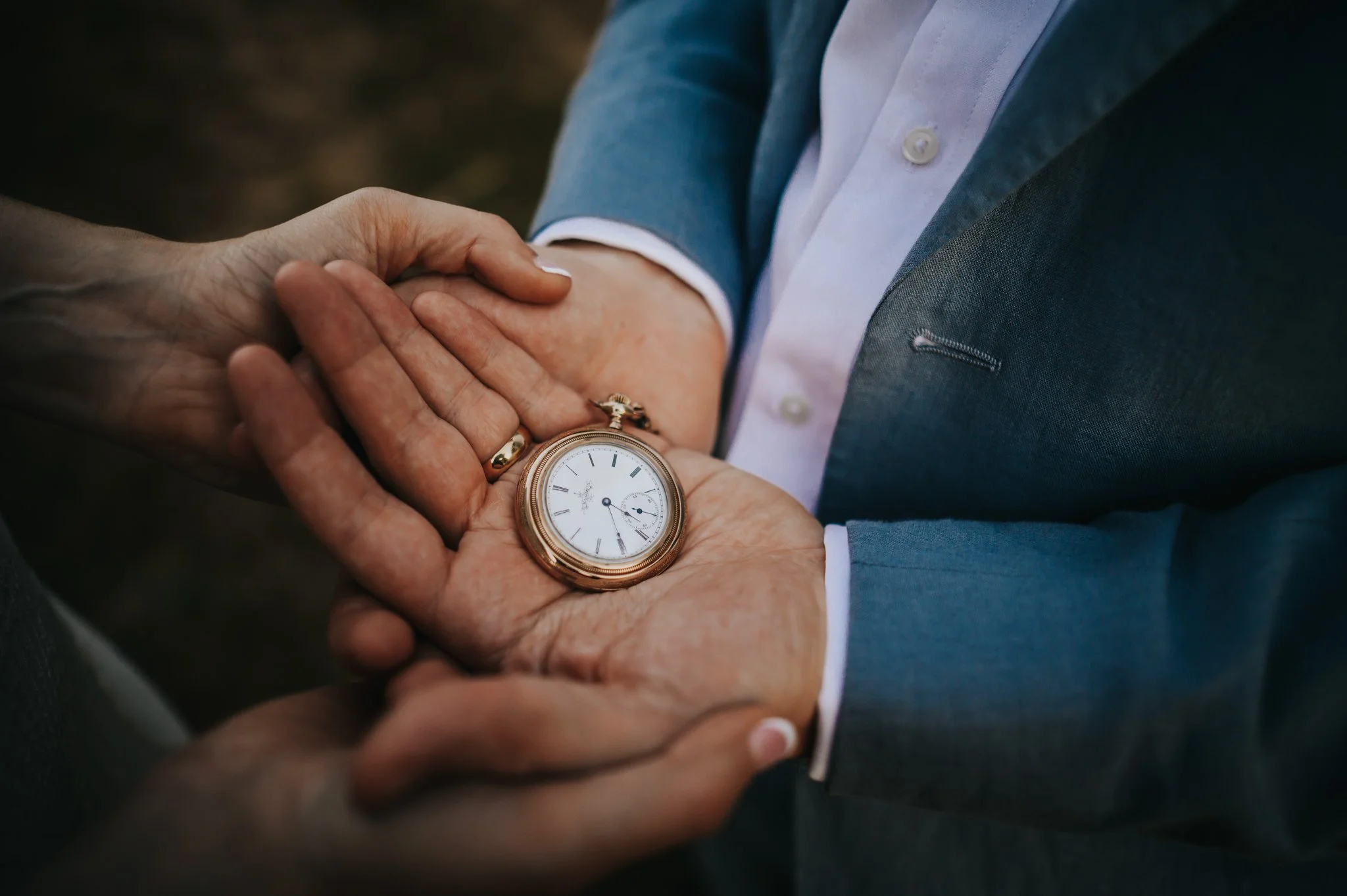 Close detail of a groom checking a pocket watch with the bride's hands resting gently on his.