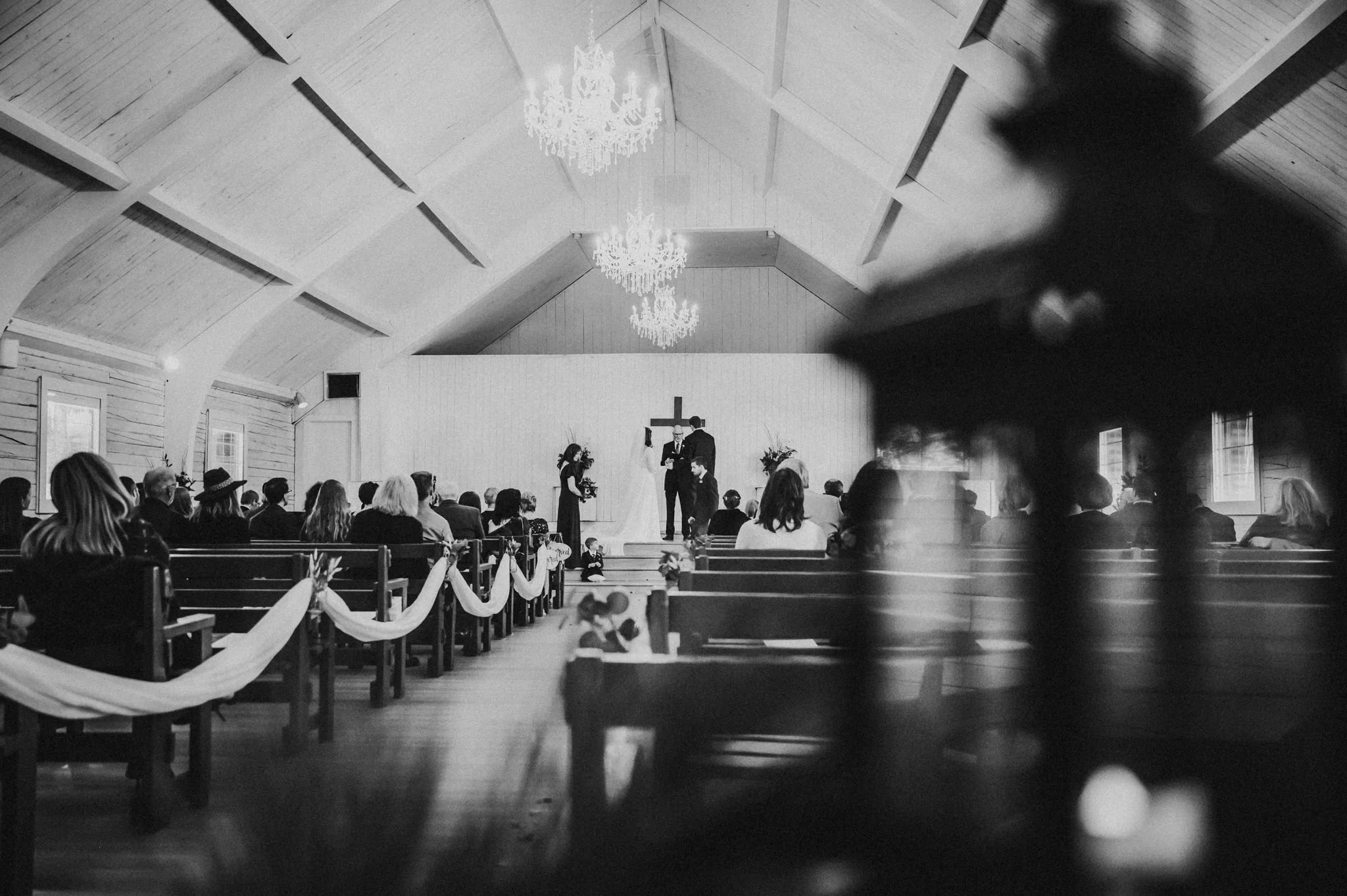 Wide black and white view of a wedding venue interior with a chandelier and ceremony seating.