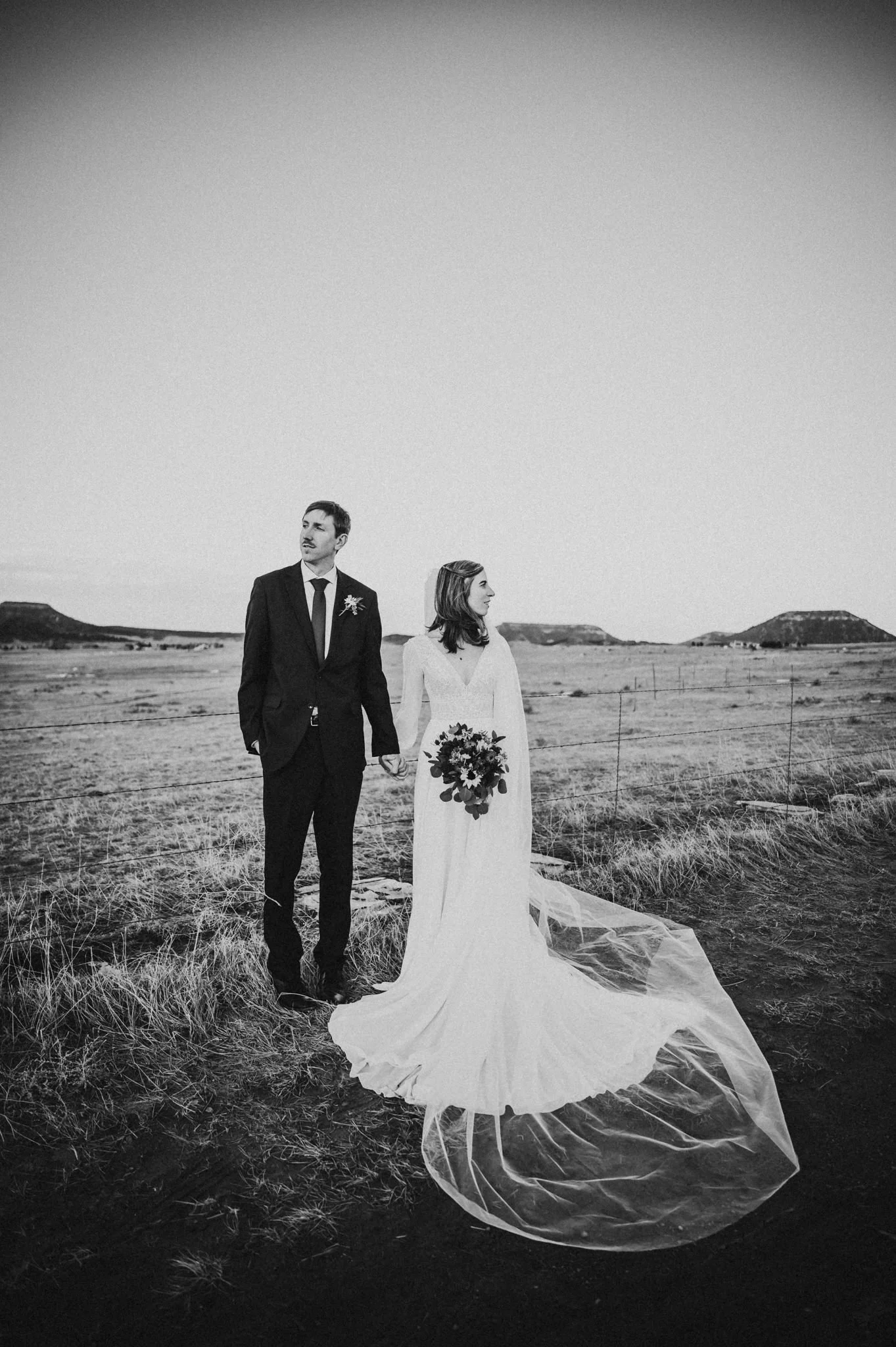 Bride and groom standing together in an open field at Pinecrest Weddings, black and white with veil flowing.