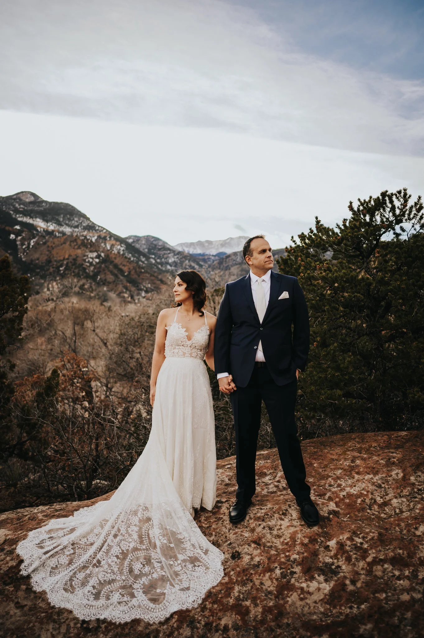 Bride and groom standing in an open mountain landscape, bride's veil catching the wind.