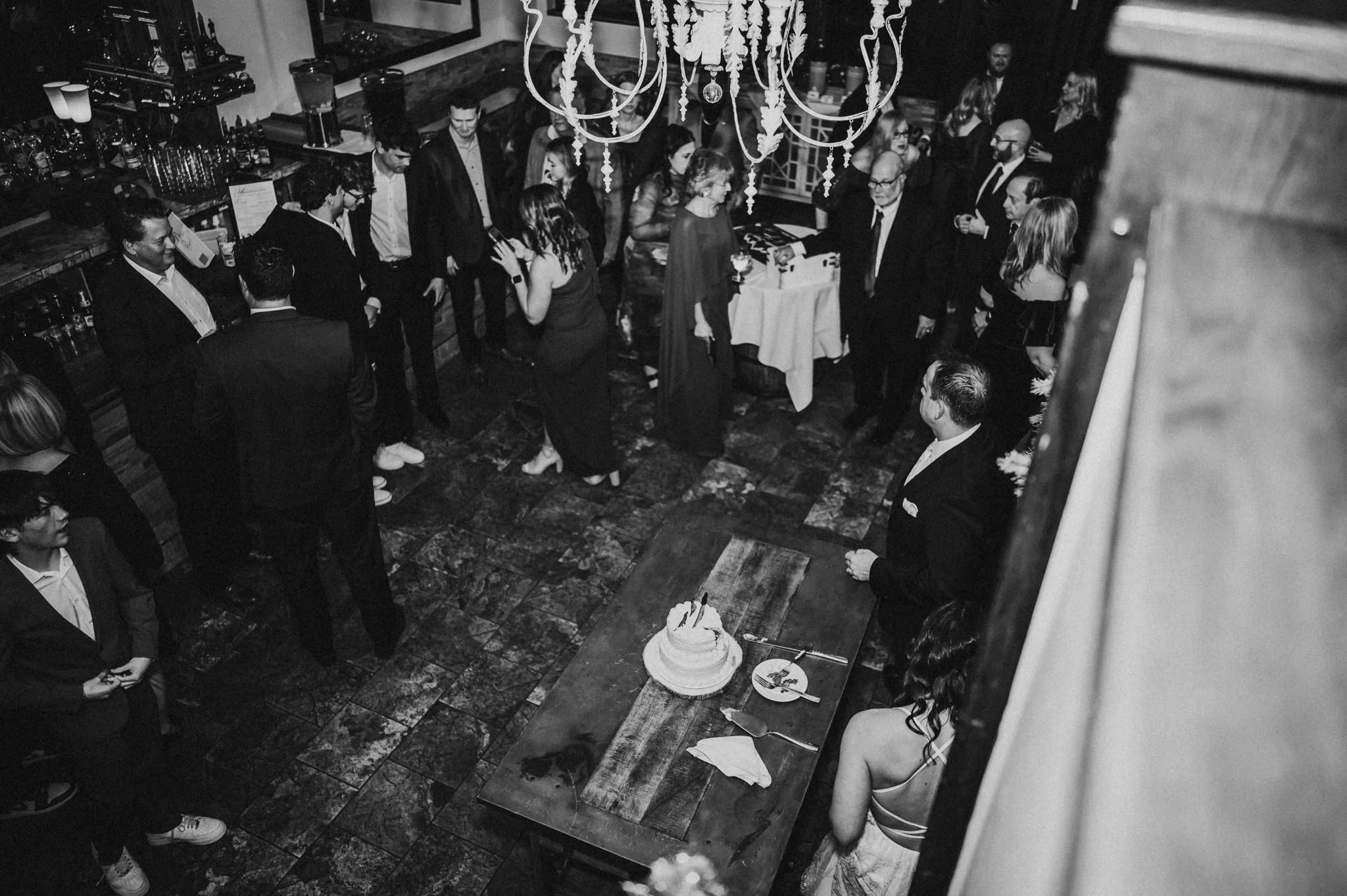 Overhead black and white view of a wedding reception dance floor with a chandelier and guests.