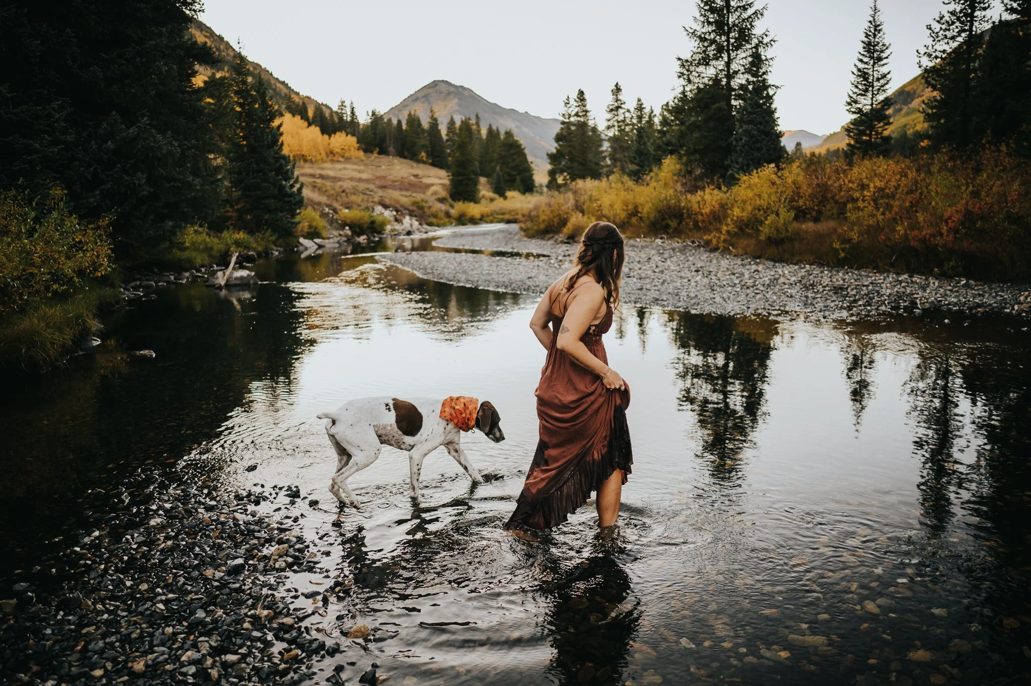 A woman explores with her dog in a stream in Crested Butte, Colorado.