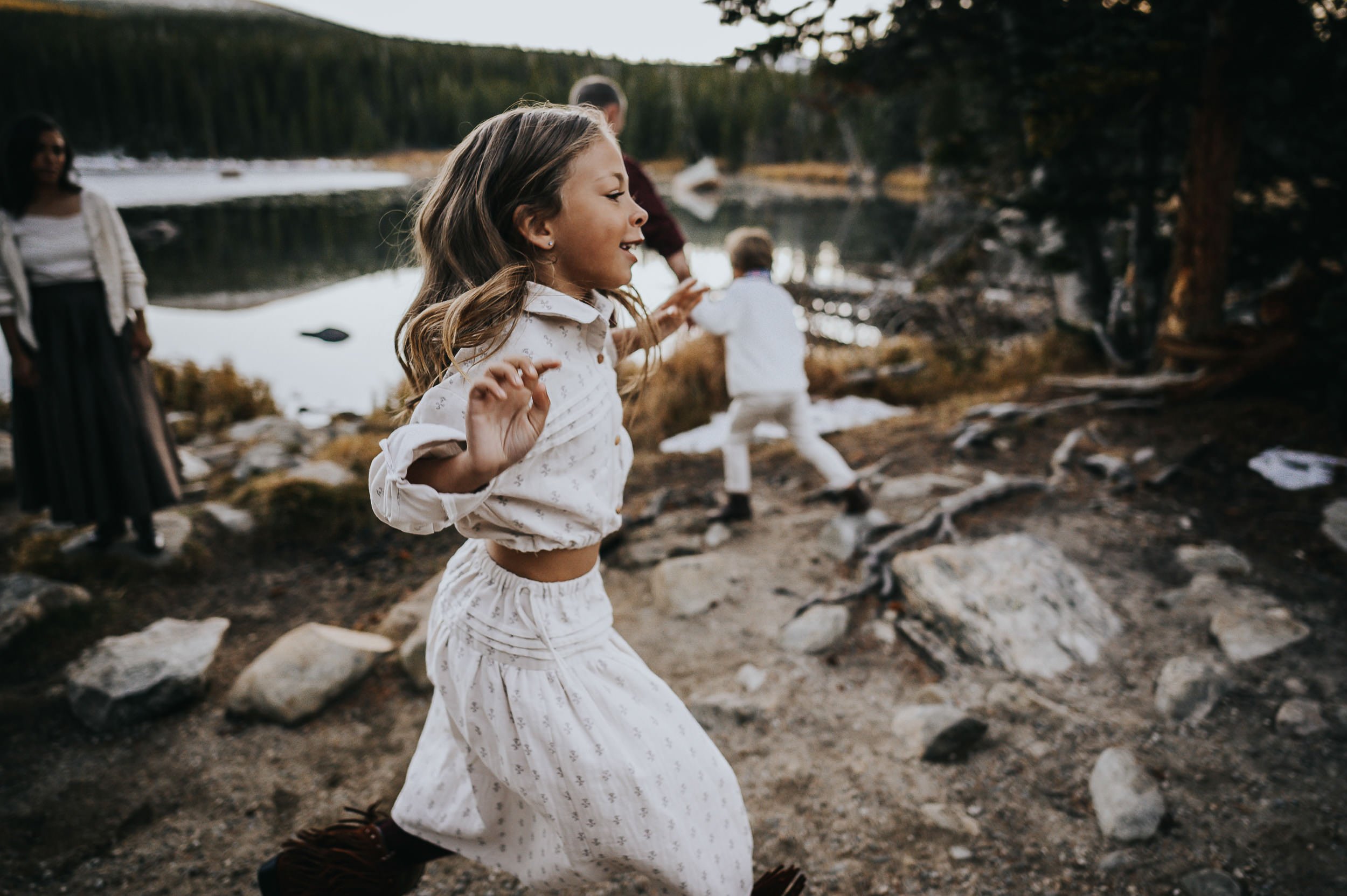 Two young children play near a alpine lake shore in Colorado, and open sky.
