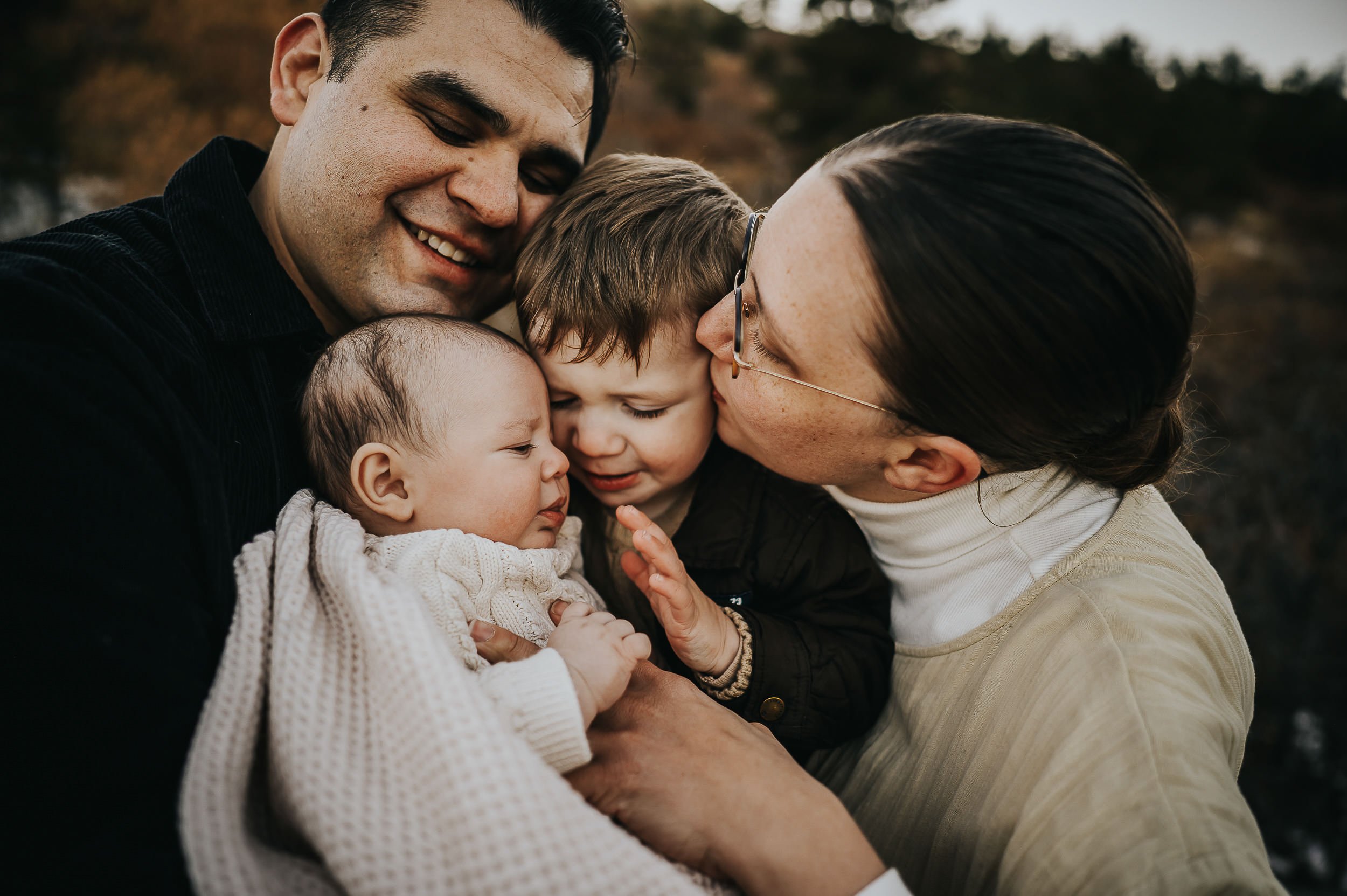 A family wearing neutral toned colors holds each other close during a family photography session in Colorado Springs.