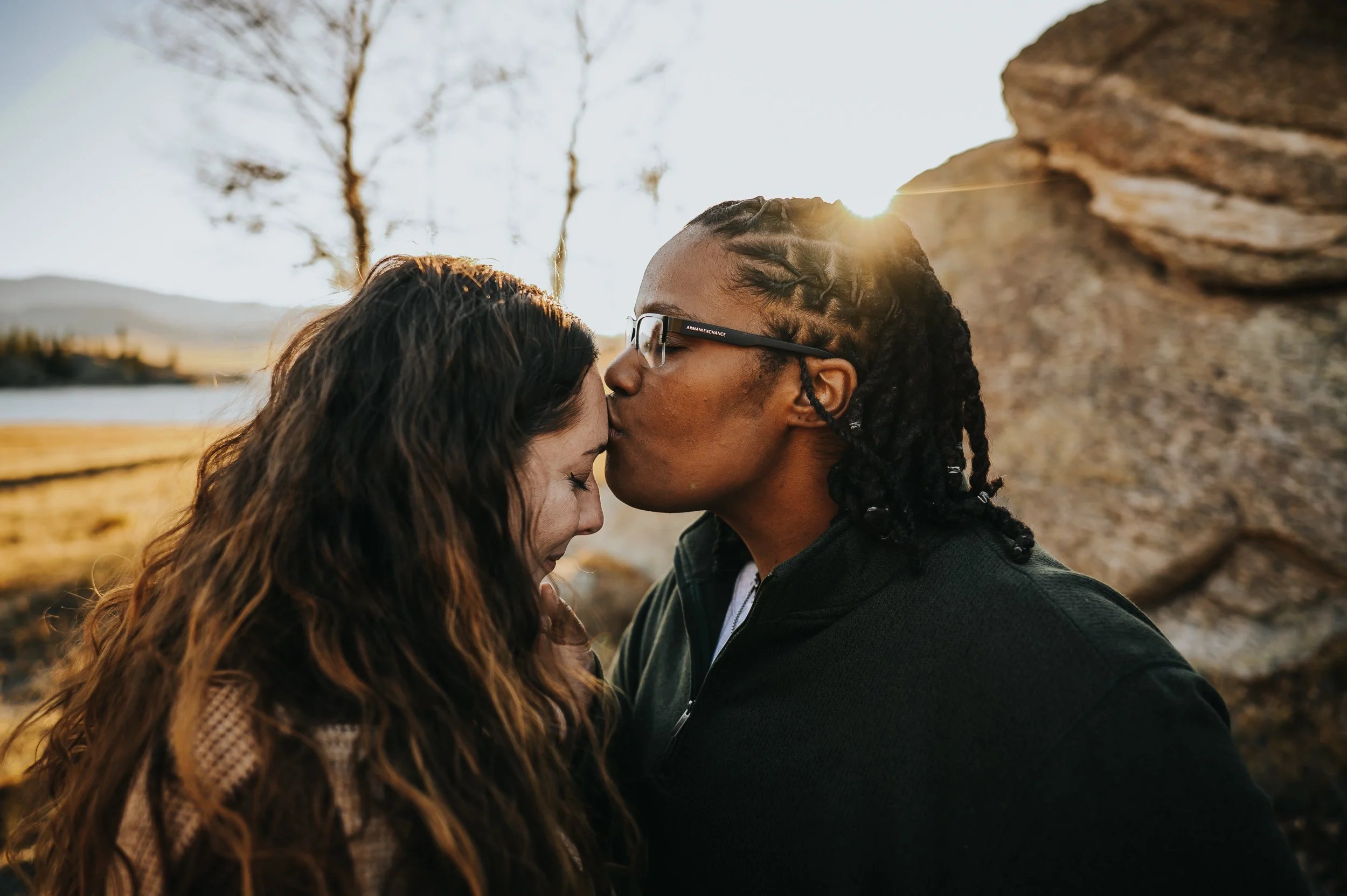Couple leaning into each other, shoulders touching, bathed in golden hour light.