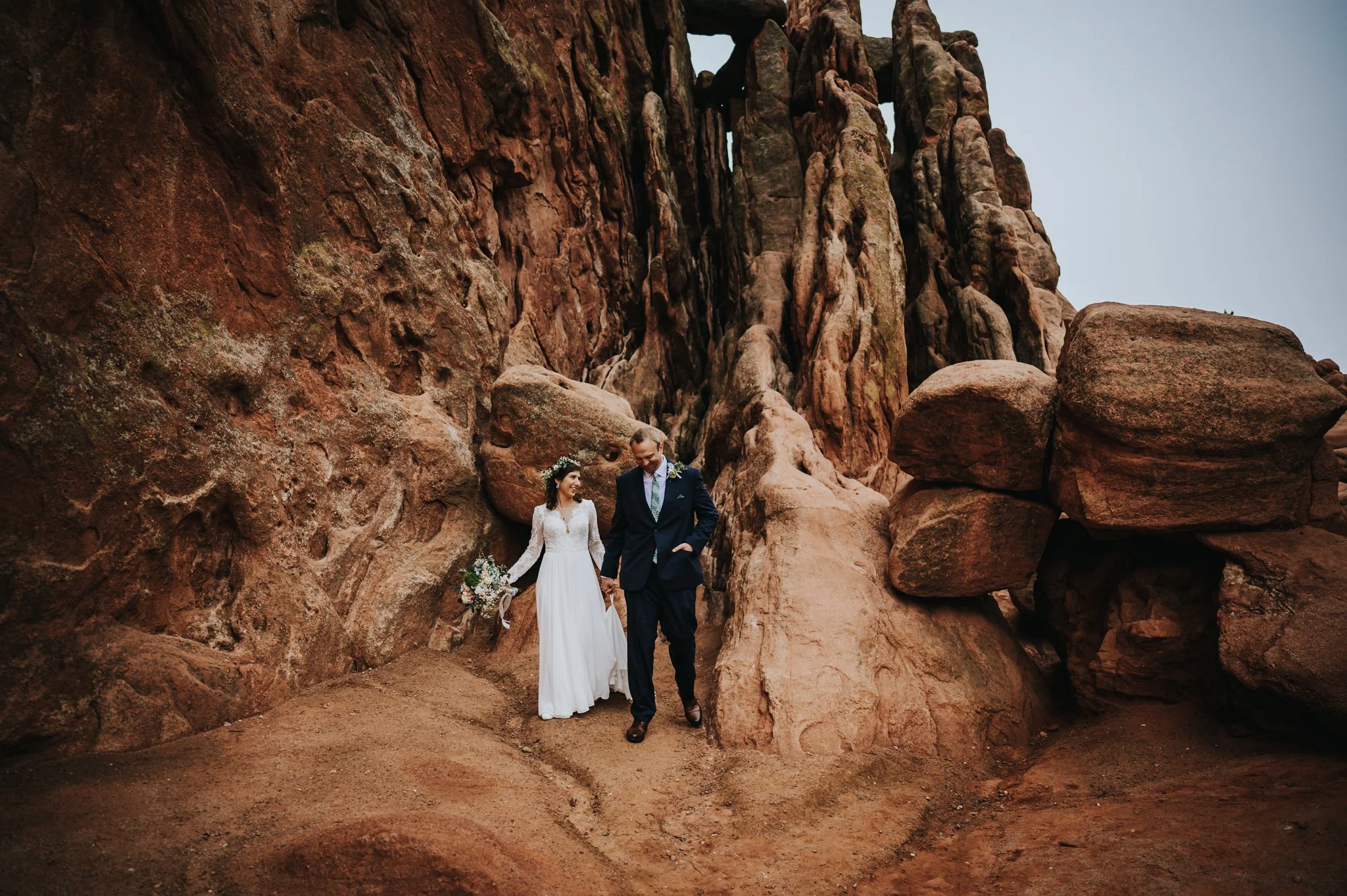 Couple walking hand in hand through a Garden of the Gods, bride in a flowing white gown.