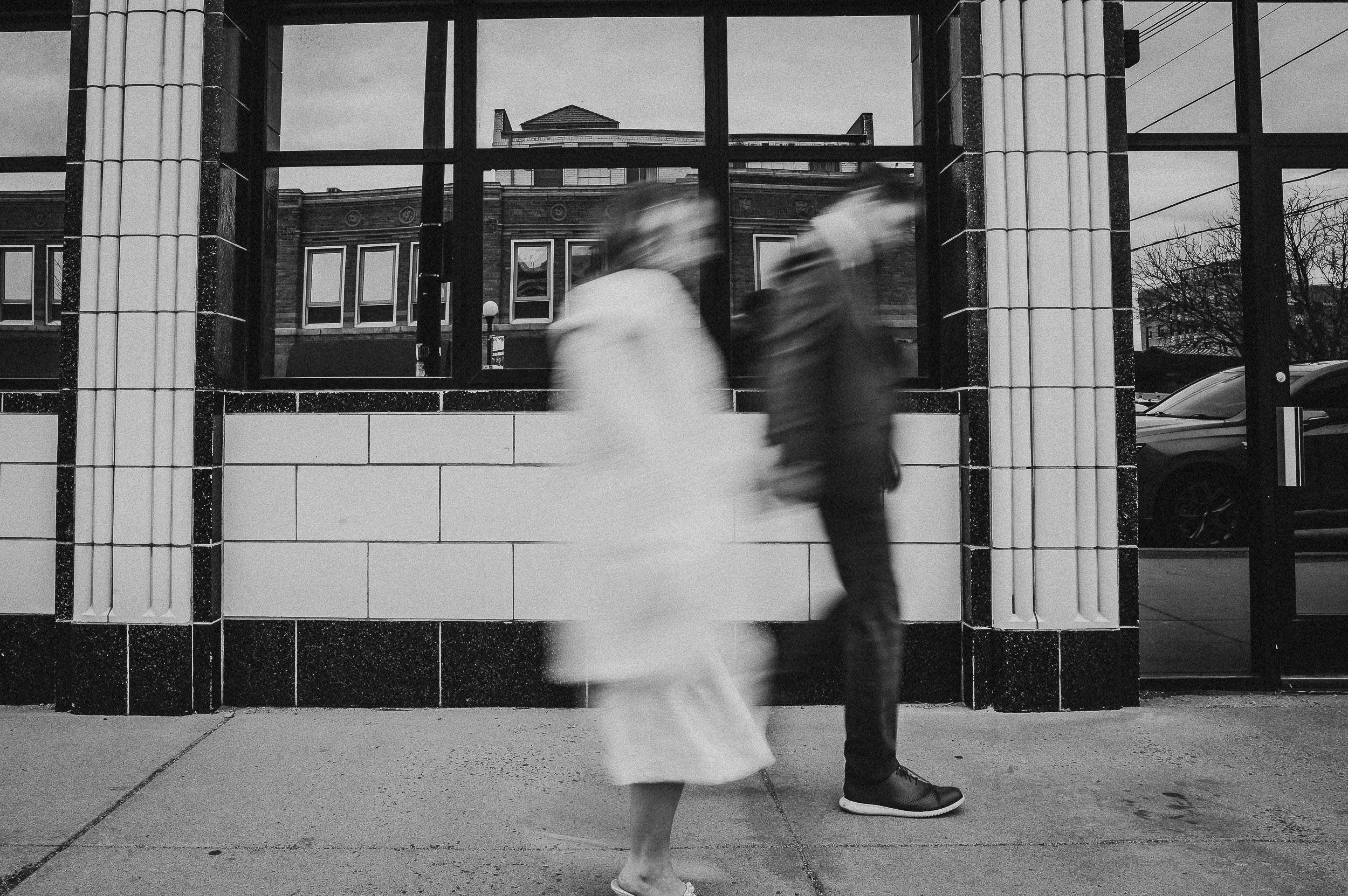 A bride and groom move through a doorway in a motion-blurred black and white portrait, architectural and editorial.