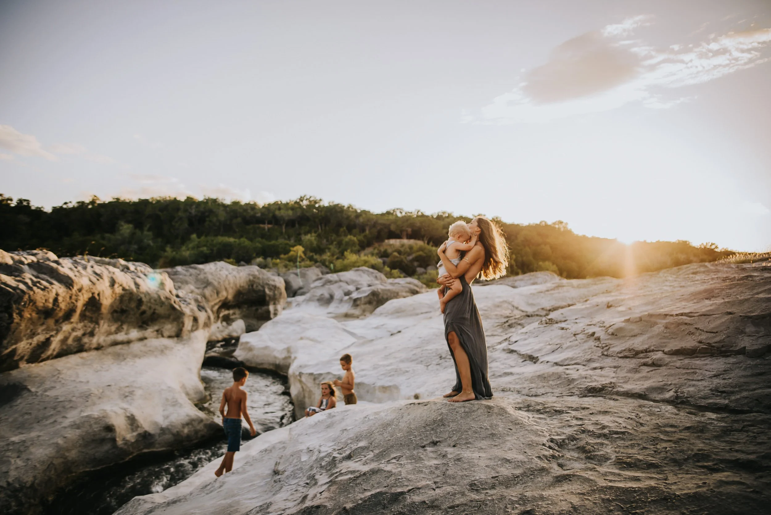 Family spread across rocky terrain at sunset, mom in gray dress, golden hour light, kids exploring the rocks.