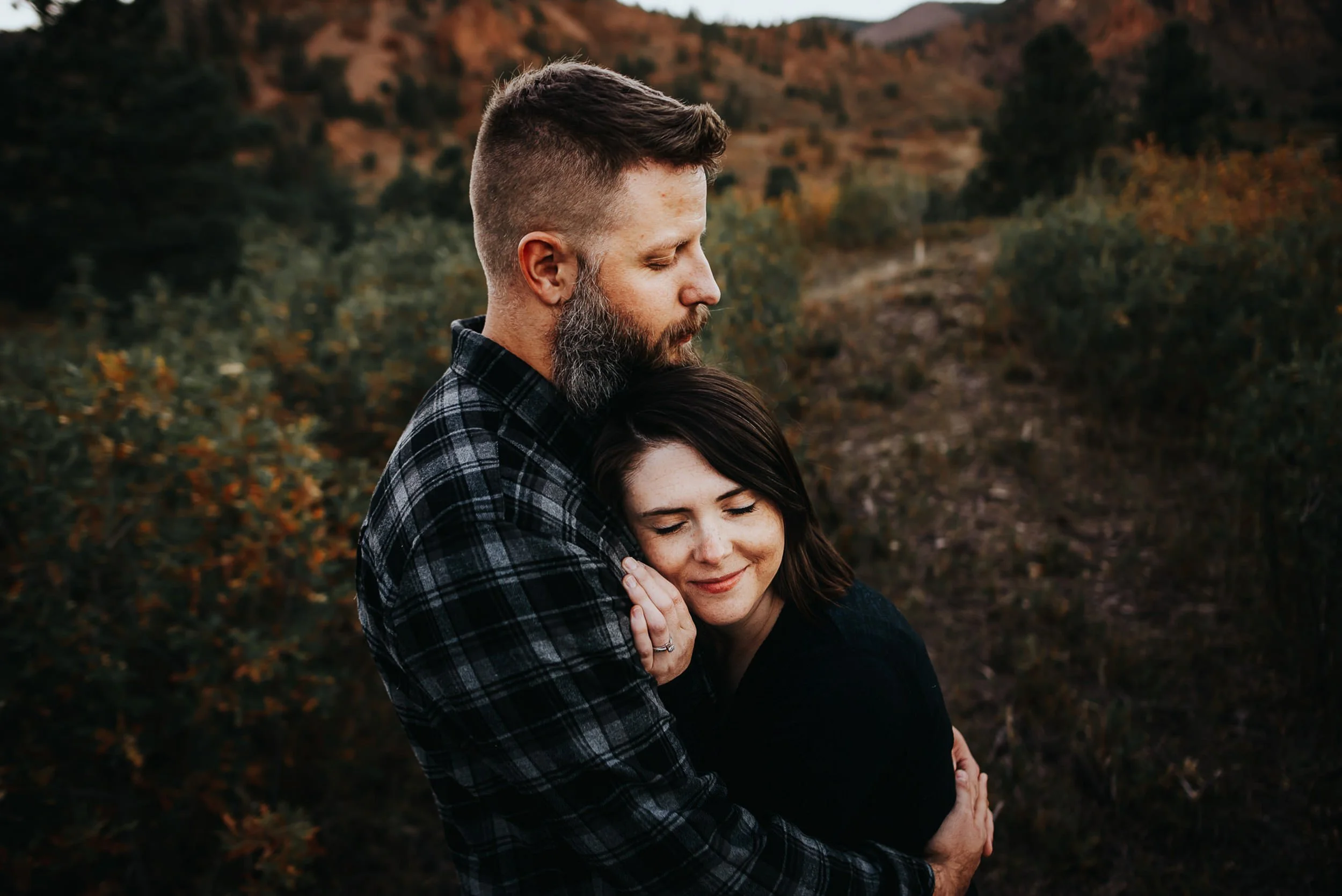 A man holds his partner from behind, both eyes closed, peaceful and intimate portrait.